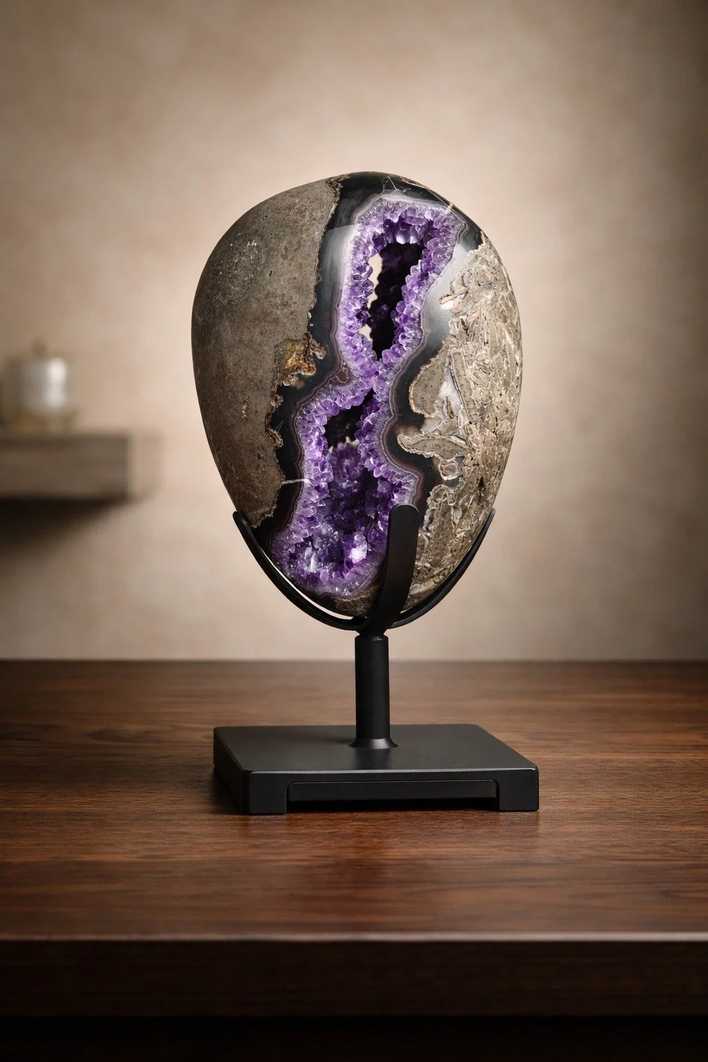 A decorative partly polished geode on a black stand with purple crystalline interior, placed on a wooden table.