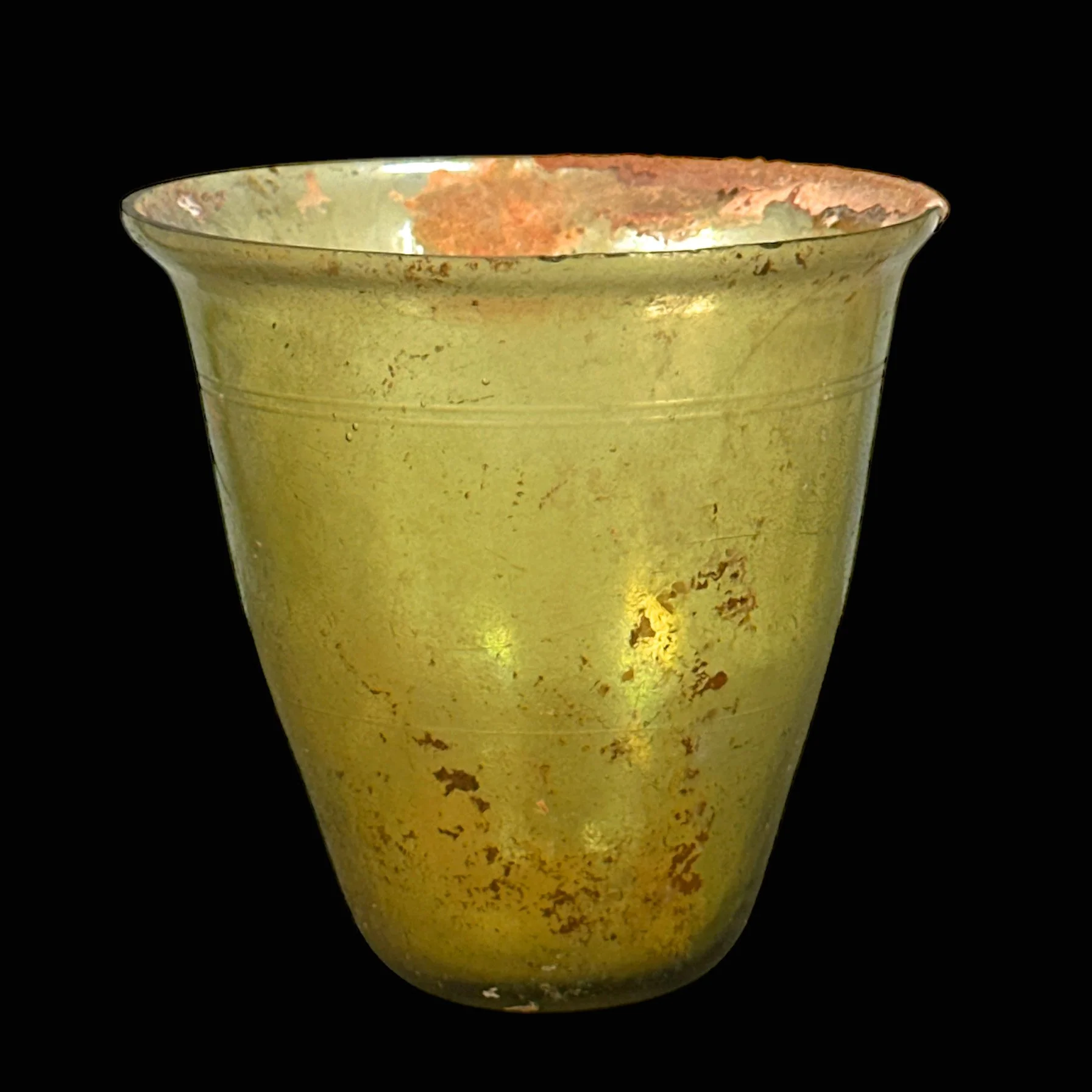 Ancient gold glass cup with wear and tarnish on a black background.