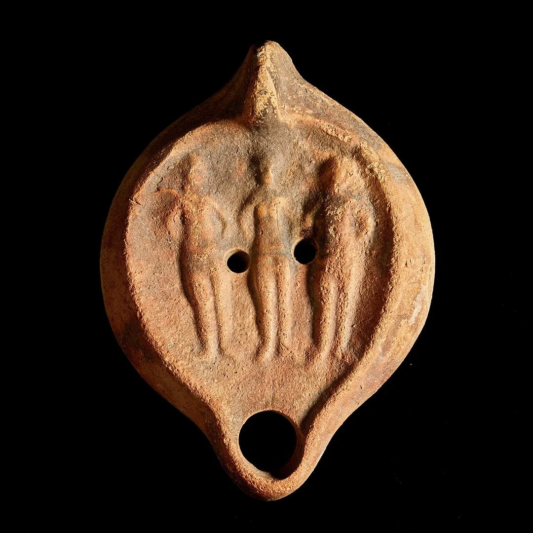 Ancient terracotta artifact with three human figures and three holes, against a black background.