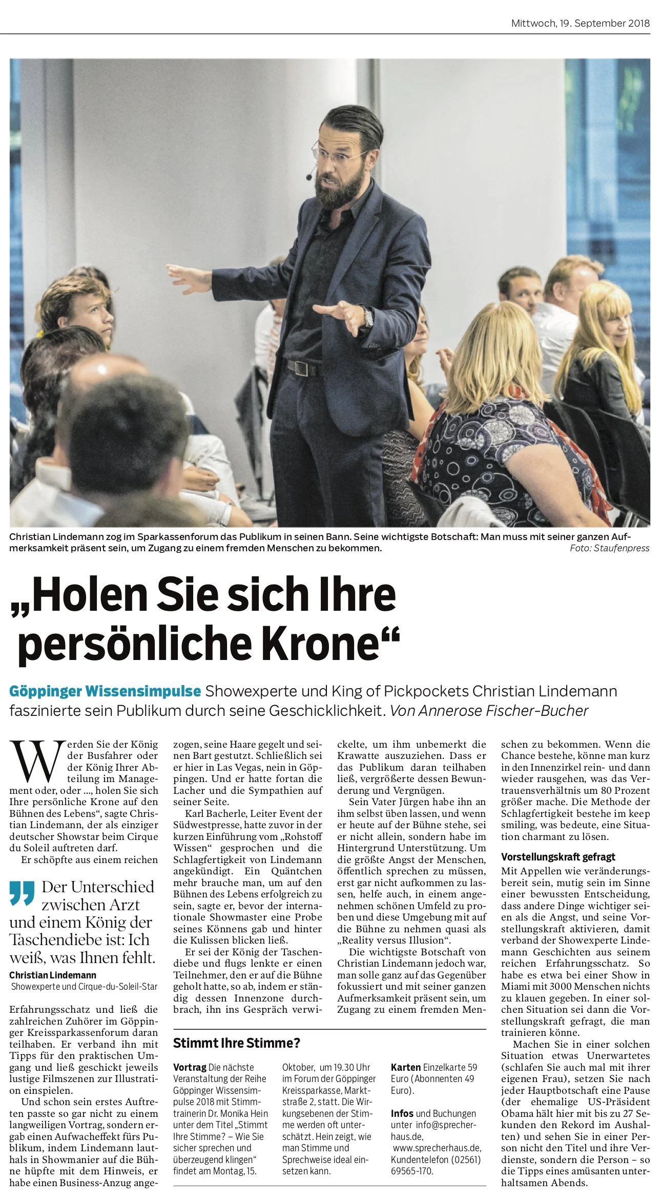 Ein Mann in dunklem Anzug hält eine Rede während einer Präsentation vor einem Publikum im Raum. Im Hintergrund sitzen Menschen, einige schauen aufmerksam, andere scheinen nachzudenken.