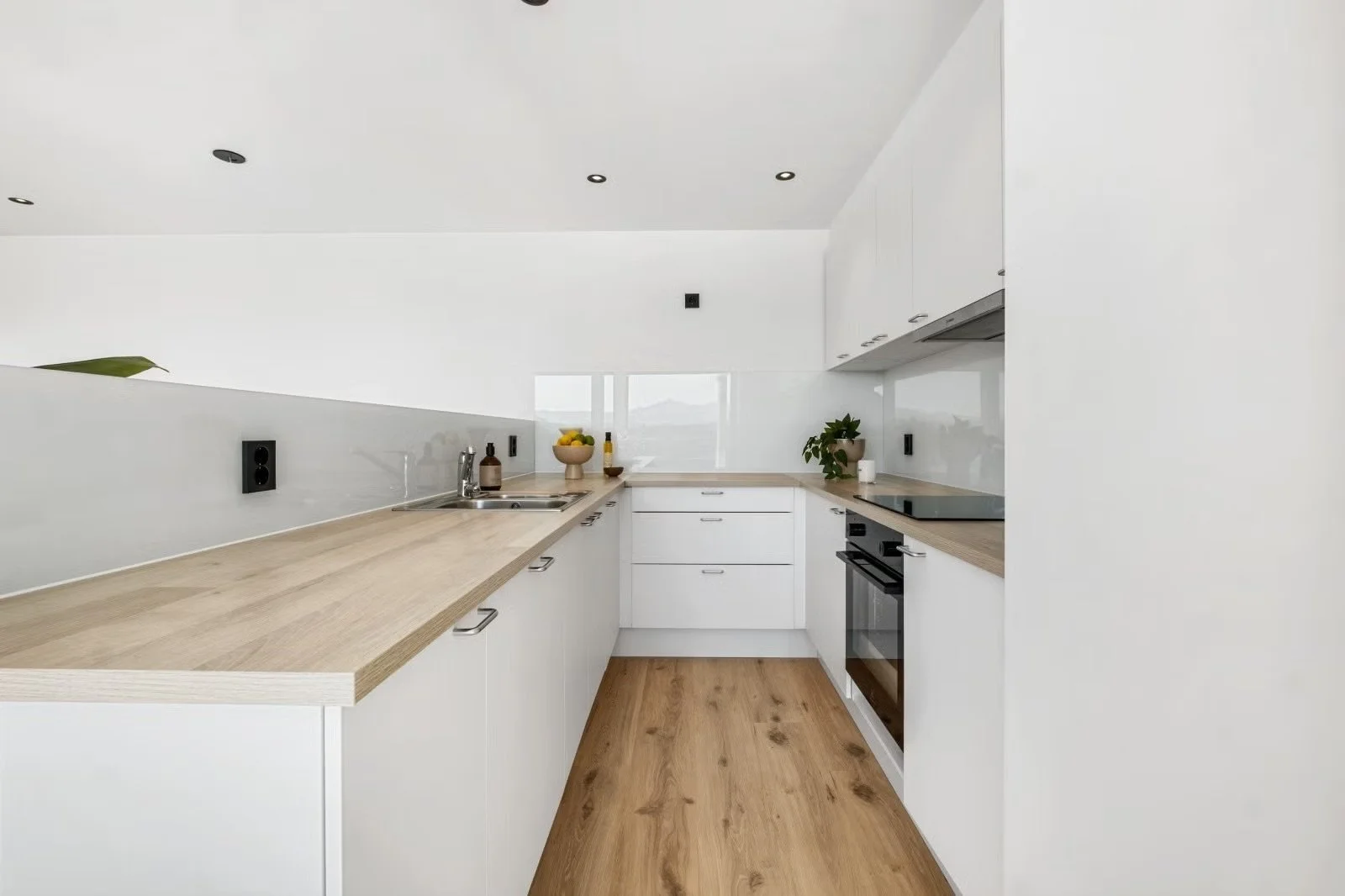 Modern kitchen with white cabinets, wooden countertops, stainless steel appliances, and minimal decor.