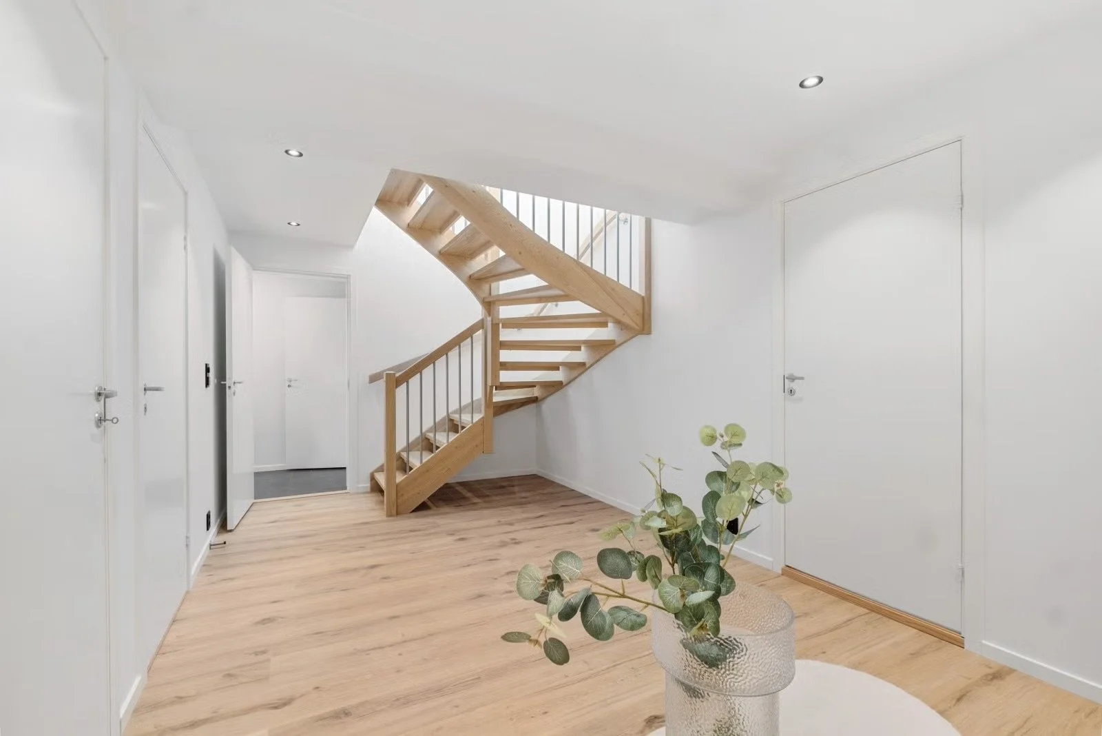 Modern white staircase with wooden steps and handrail in a bright, minimalist interior with hardwood floors and a potted plant.