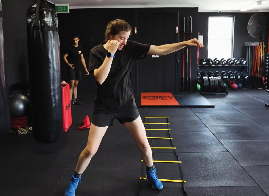 A woman with a headband practicing boxing with a punching bag in a gym.