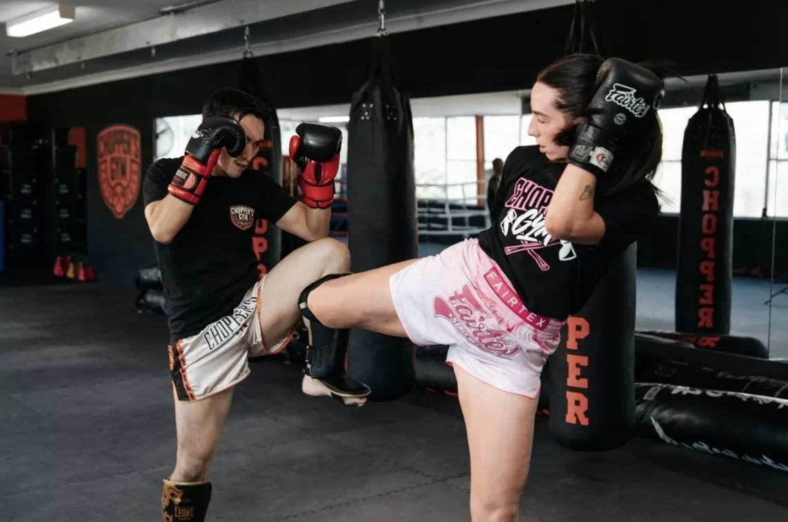 Group of people in a gym practicing boxing or kickboxing, standing in a line with fists up, wearing gloves, in a training session.