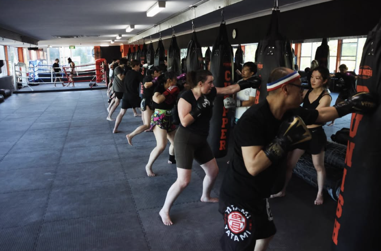 People participating in a martial arts class, practicing punching techniques on hanging black punching bags in a spacious training room.