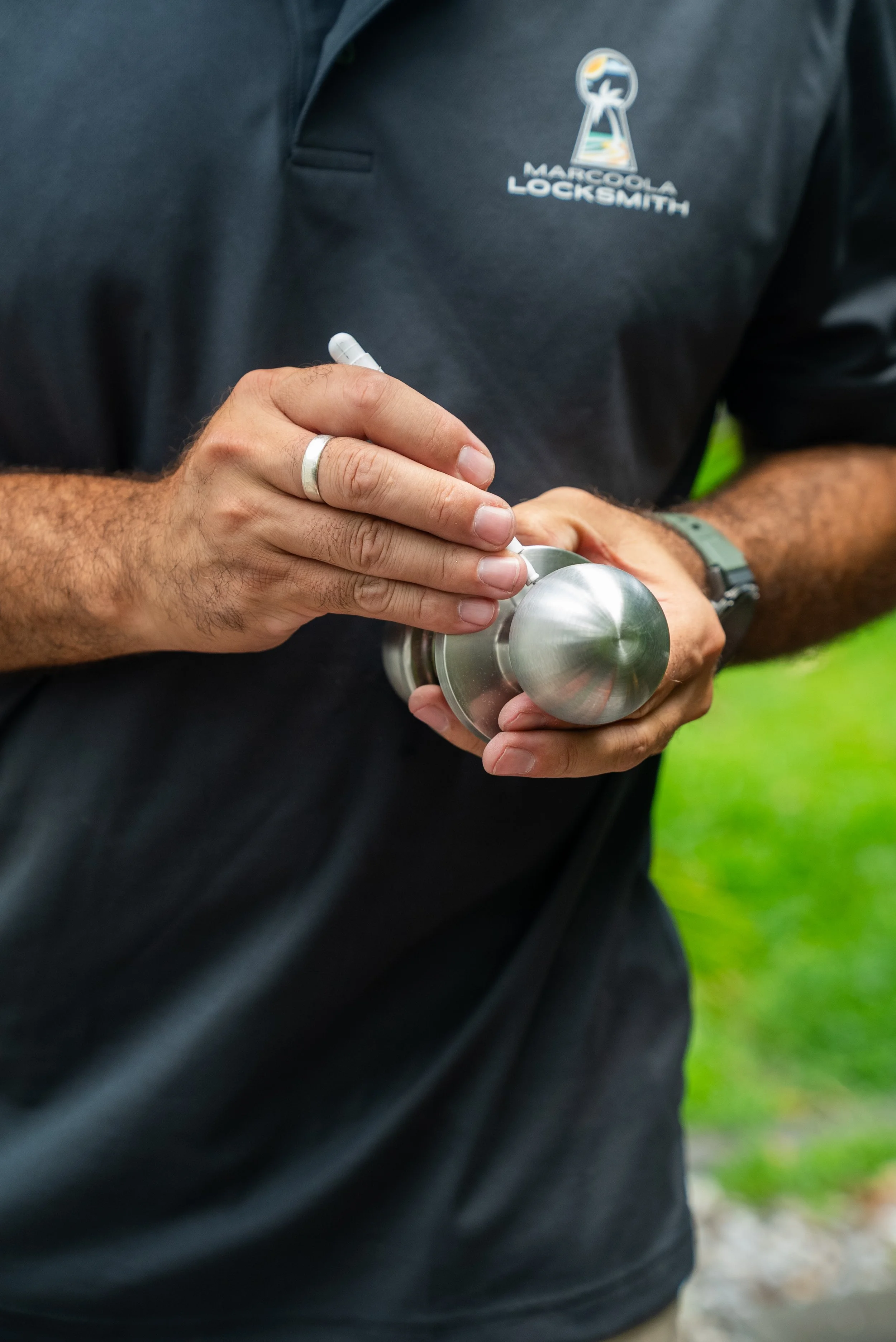 A person wearing a black shirt with a logo that says "Marcoola Locksmith" holds a stainless steel water bottle and a pen in their hands.