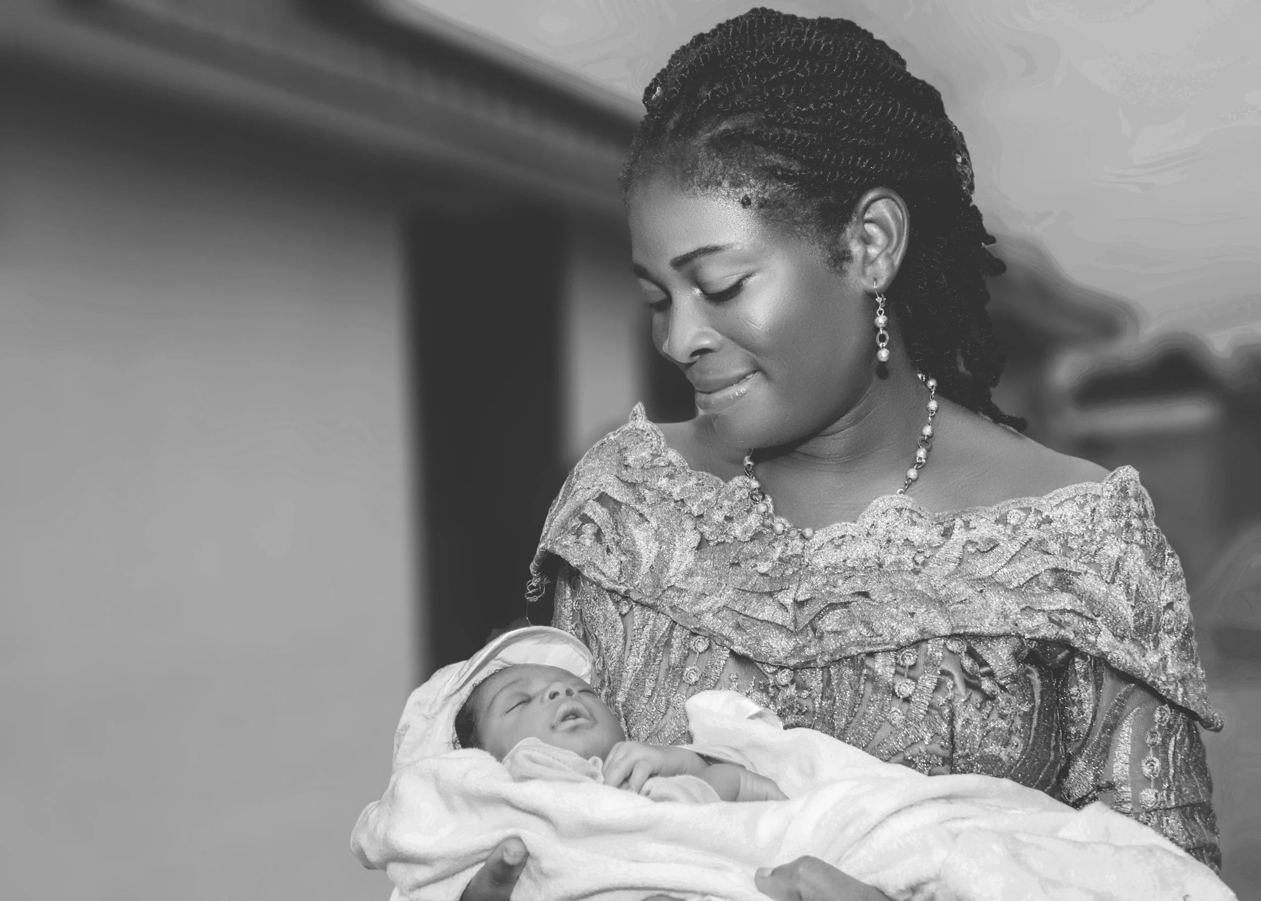 A black and white photo of a woman smiling down at a sleeping baby wrapped in a blanket she is holding.