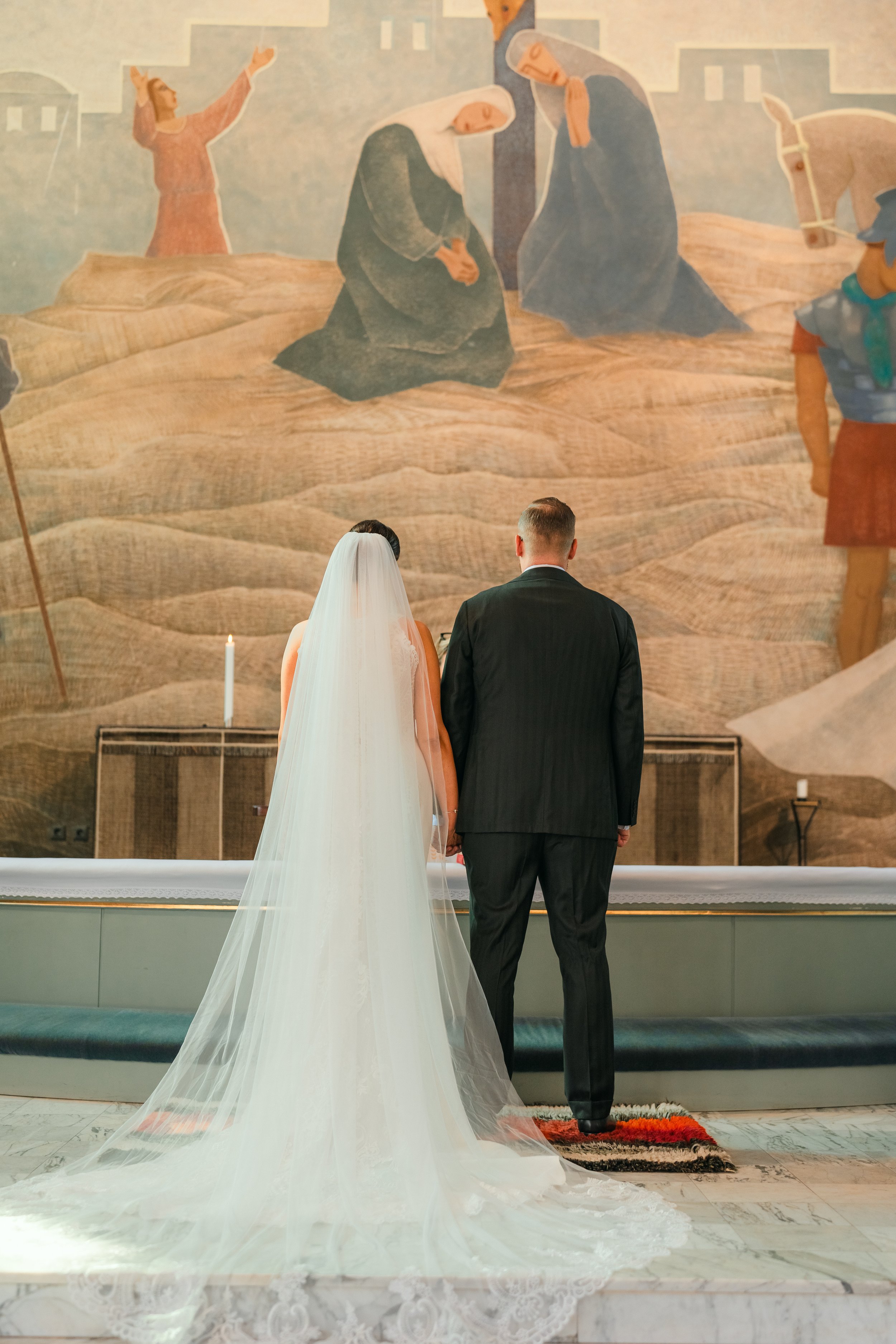 Bride and groom standing at altar with mural backdrop in a church.