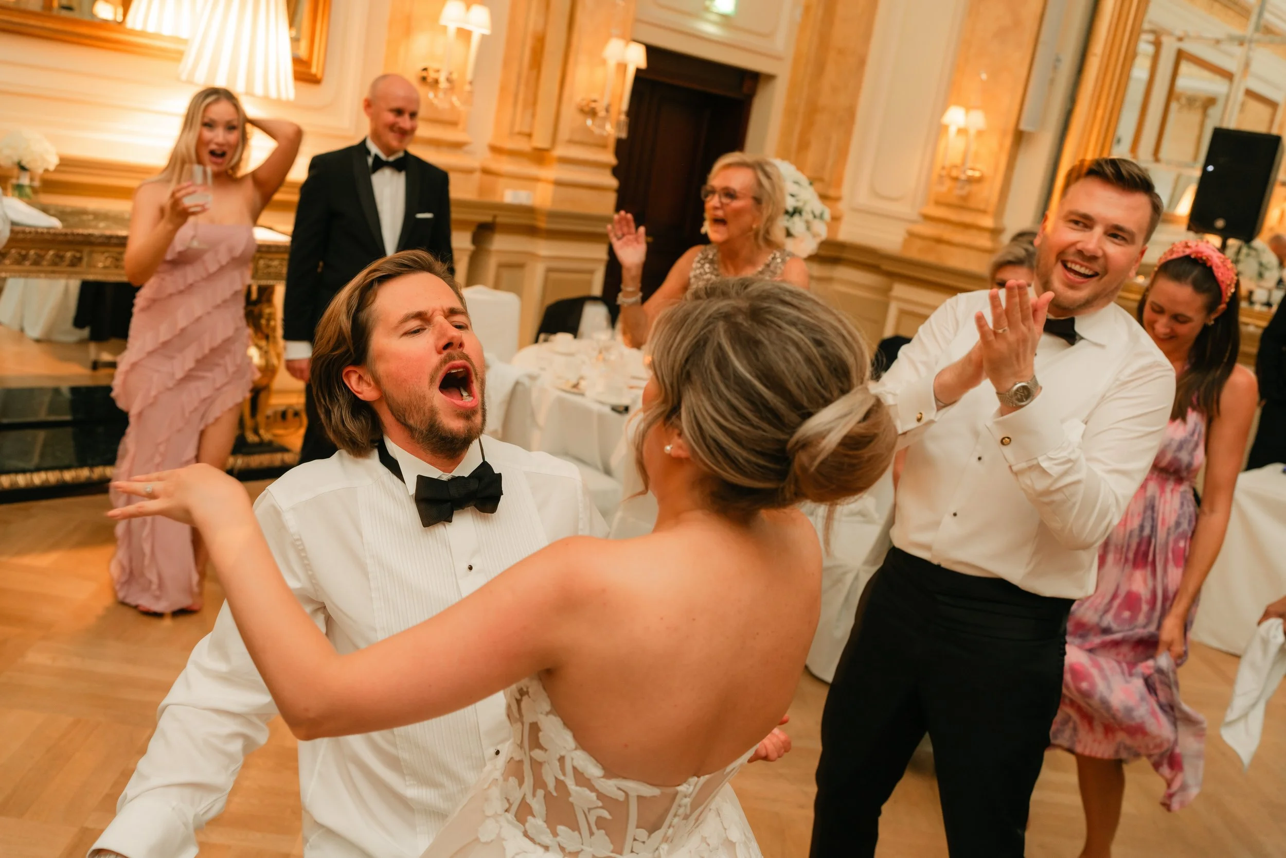 Wedding party, guests in formal attire dancing and celebrating indoors.