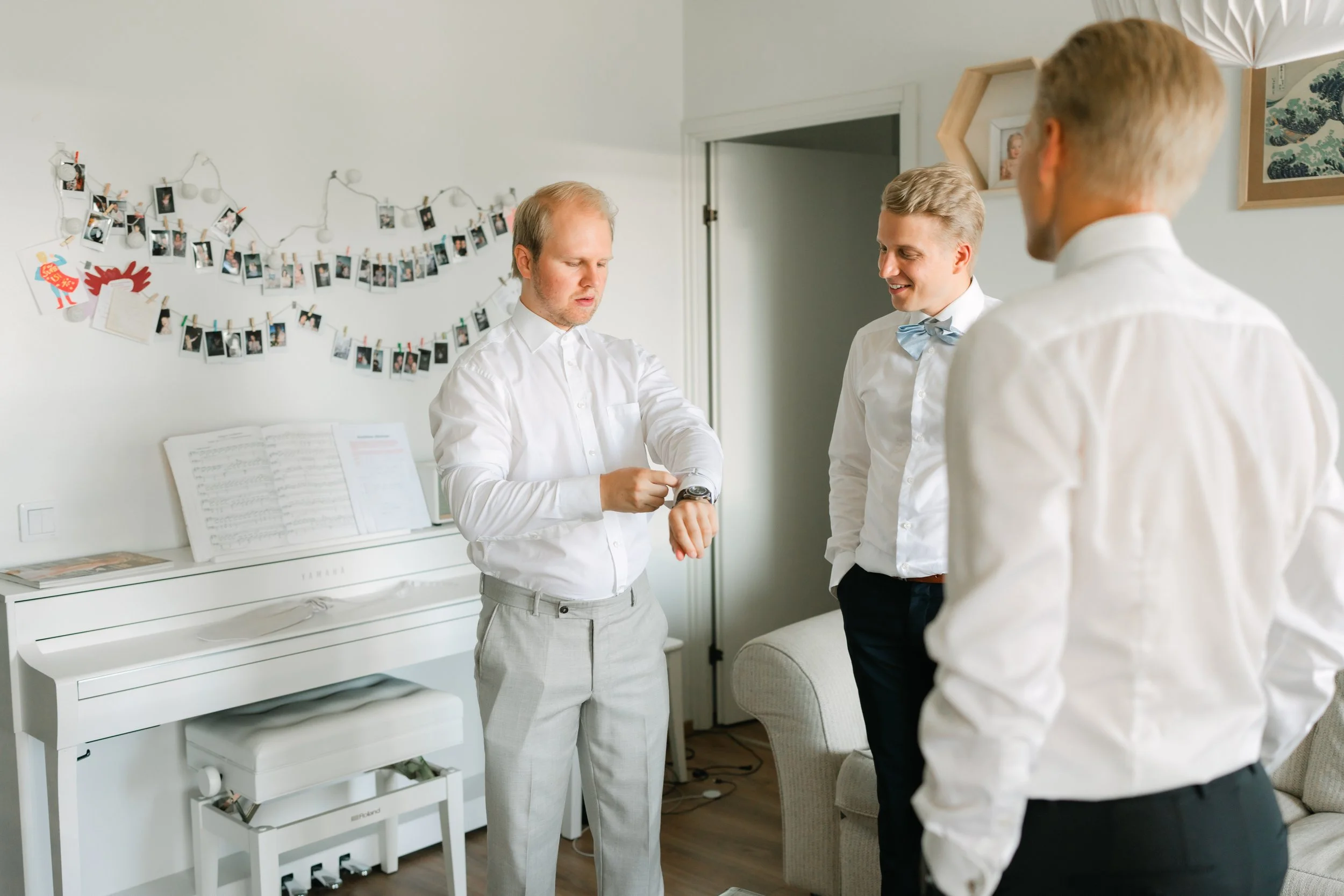 Three men in formal attire standing in a room with a piano and photo decorations.