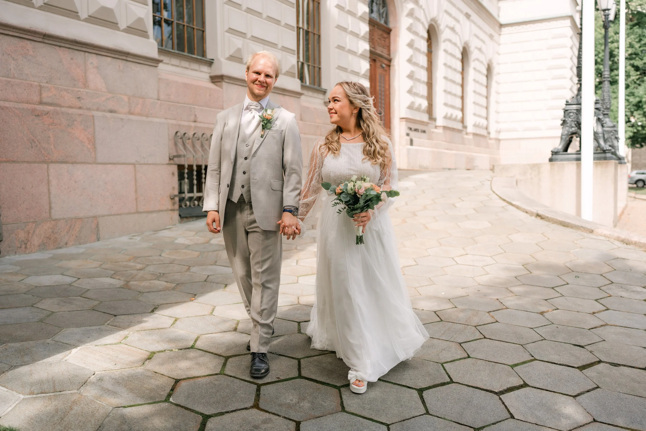 Bride and groom walking outdoors, holding hands, wedding attire