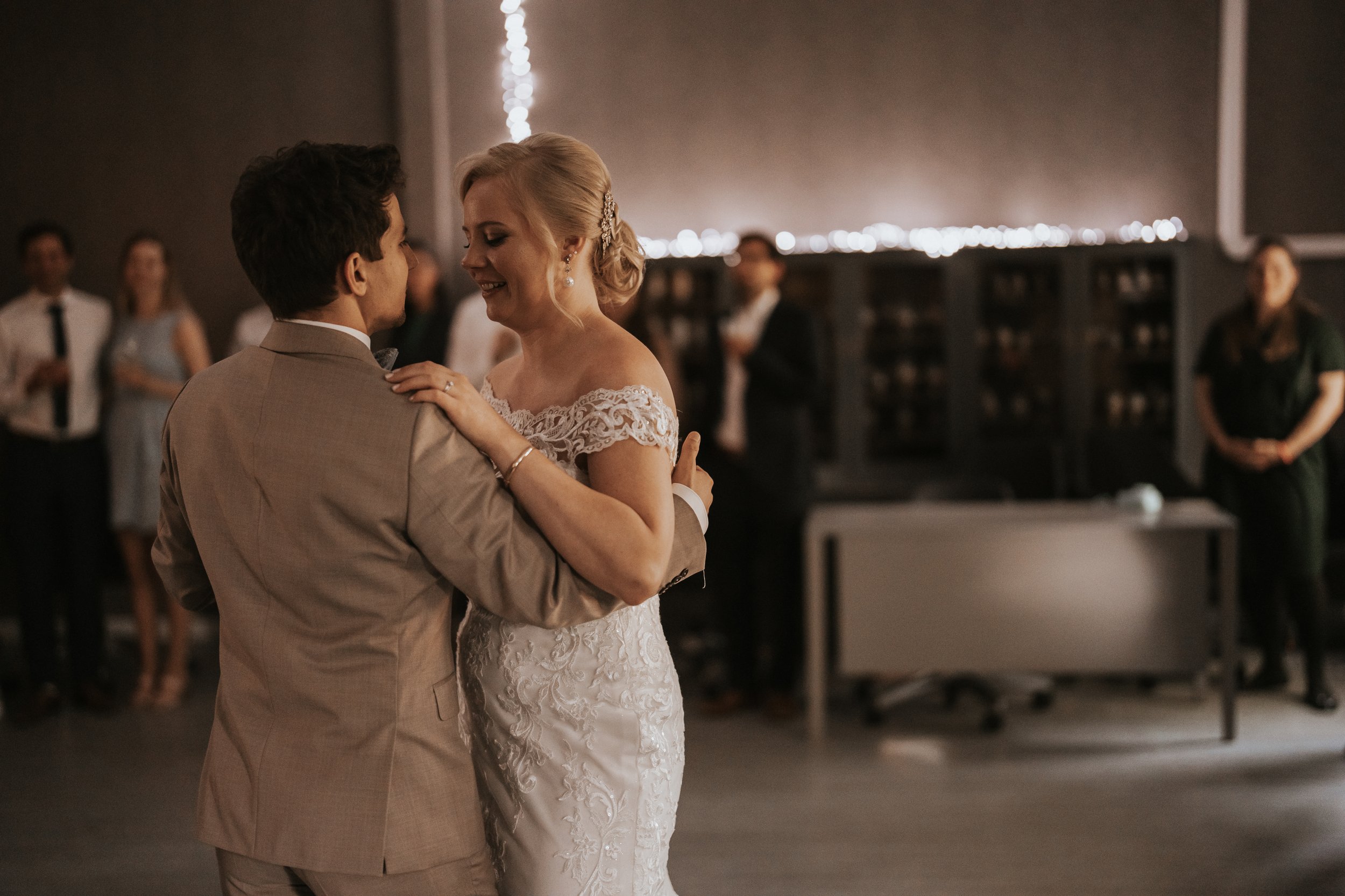 Bride and groom dancing at wedding reception, guests in background.