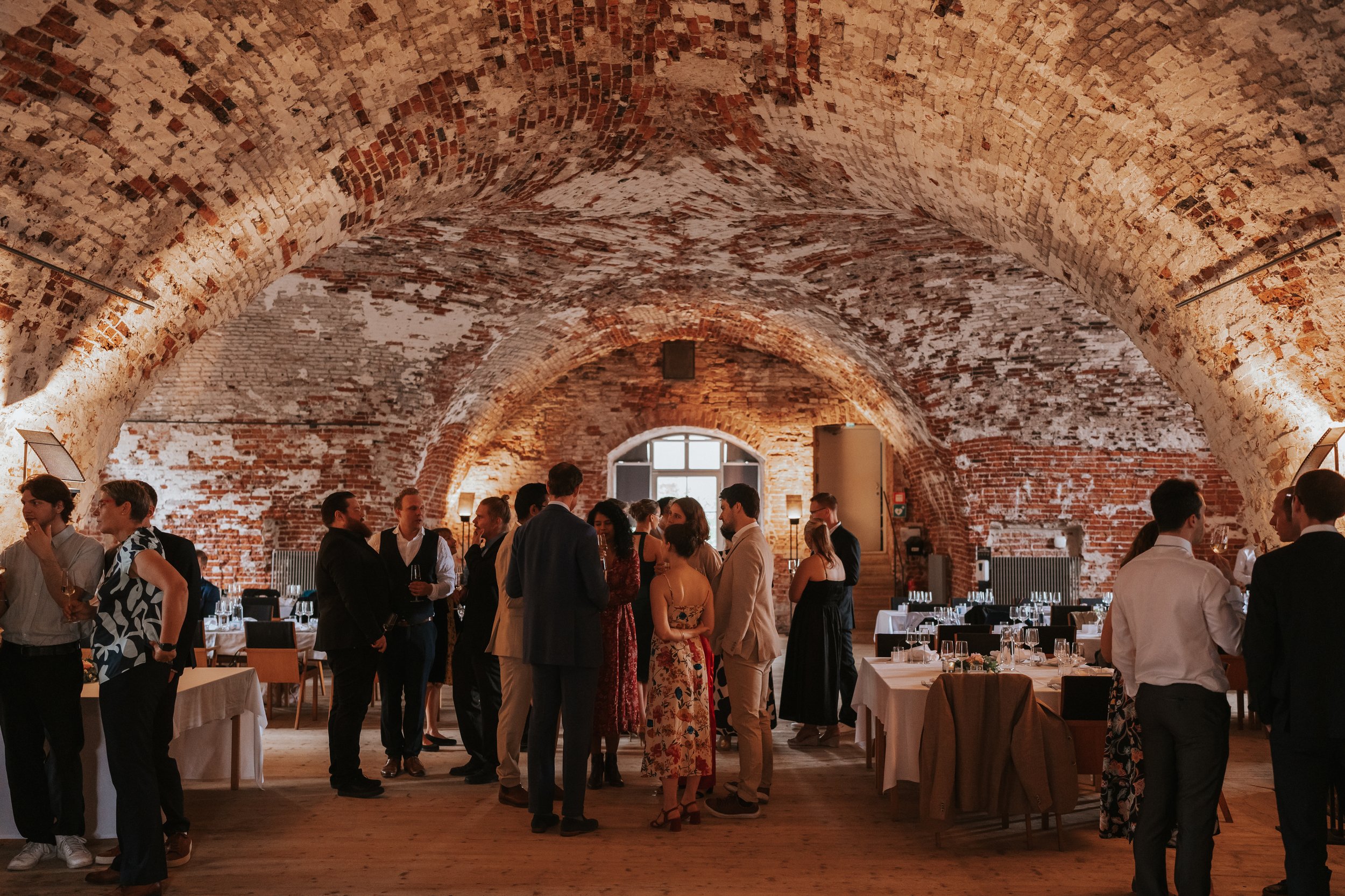 People socializing at an event in a rustic brick vaulted room.