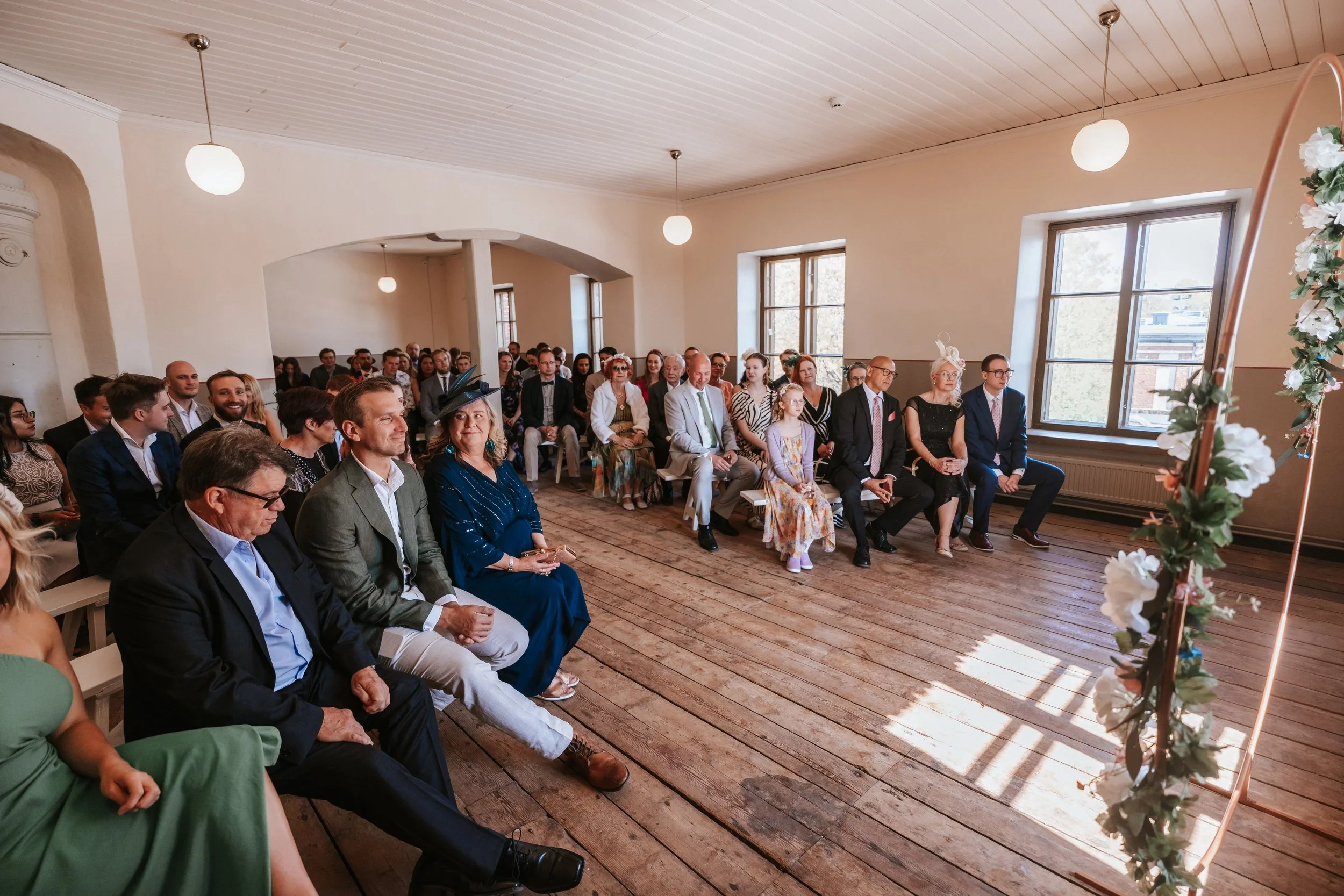 Indoor wedding ceremony with guests seated, floral decorations in foreground