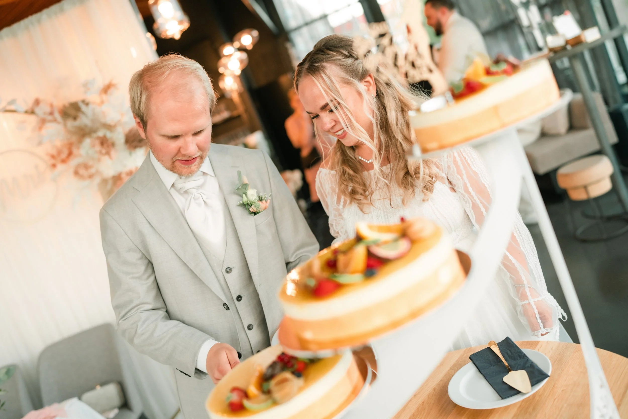 Wedding couple cutting multi-tiered fruit-topped cake at reception venue.