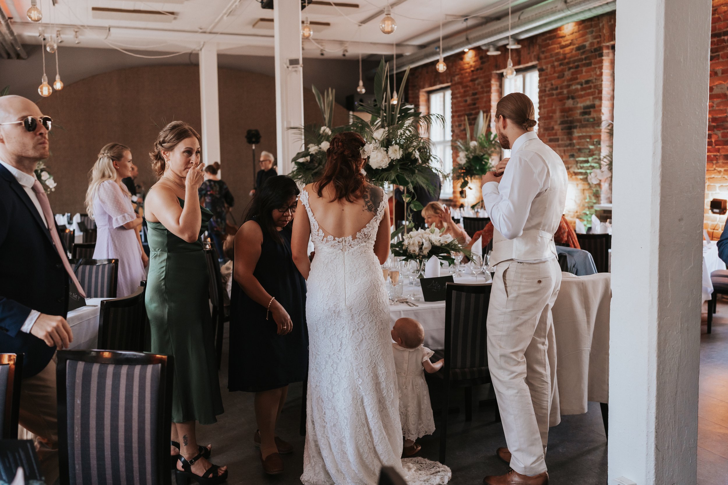 Wedding reception with bride in white dress, guests in elegant attire, and floral decorations.