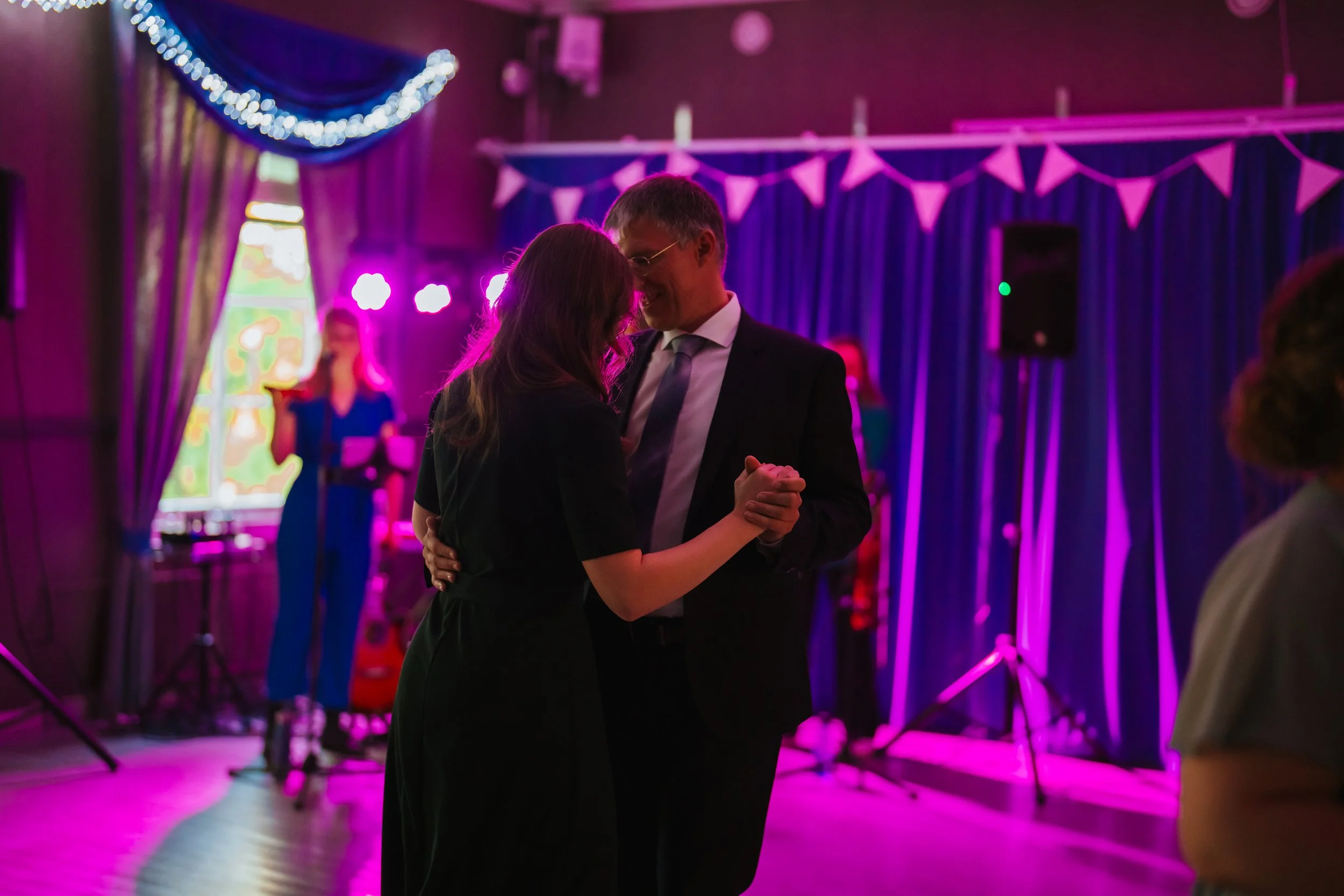 Couple dancing at a party with purple lighting and blue curtains