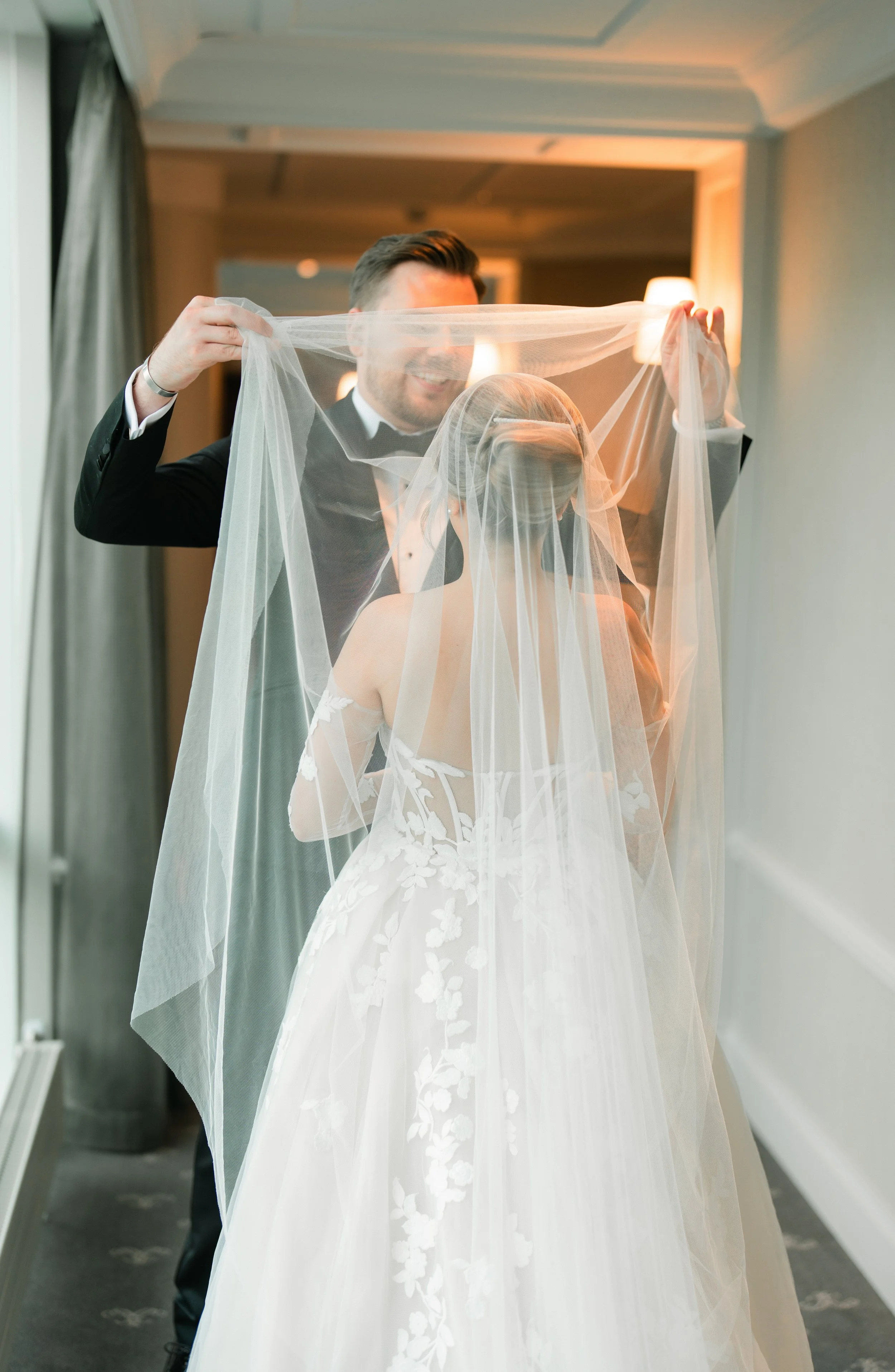 Bride and groom during wedding ceremony, groom lifting bride's veil, bride wearing a lace gown with floral patterns.
