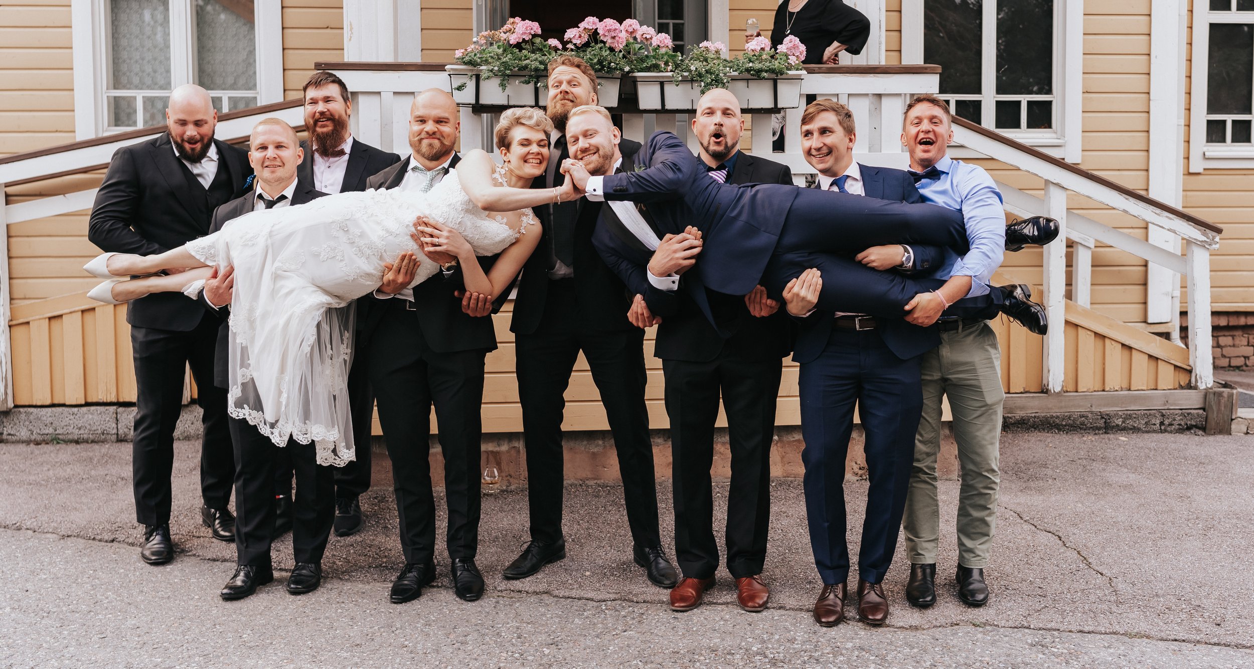 Group of people holding a bride and groom in a playful wedding photo, outdoors.