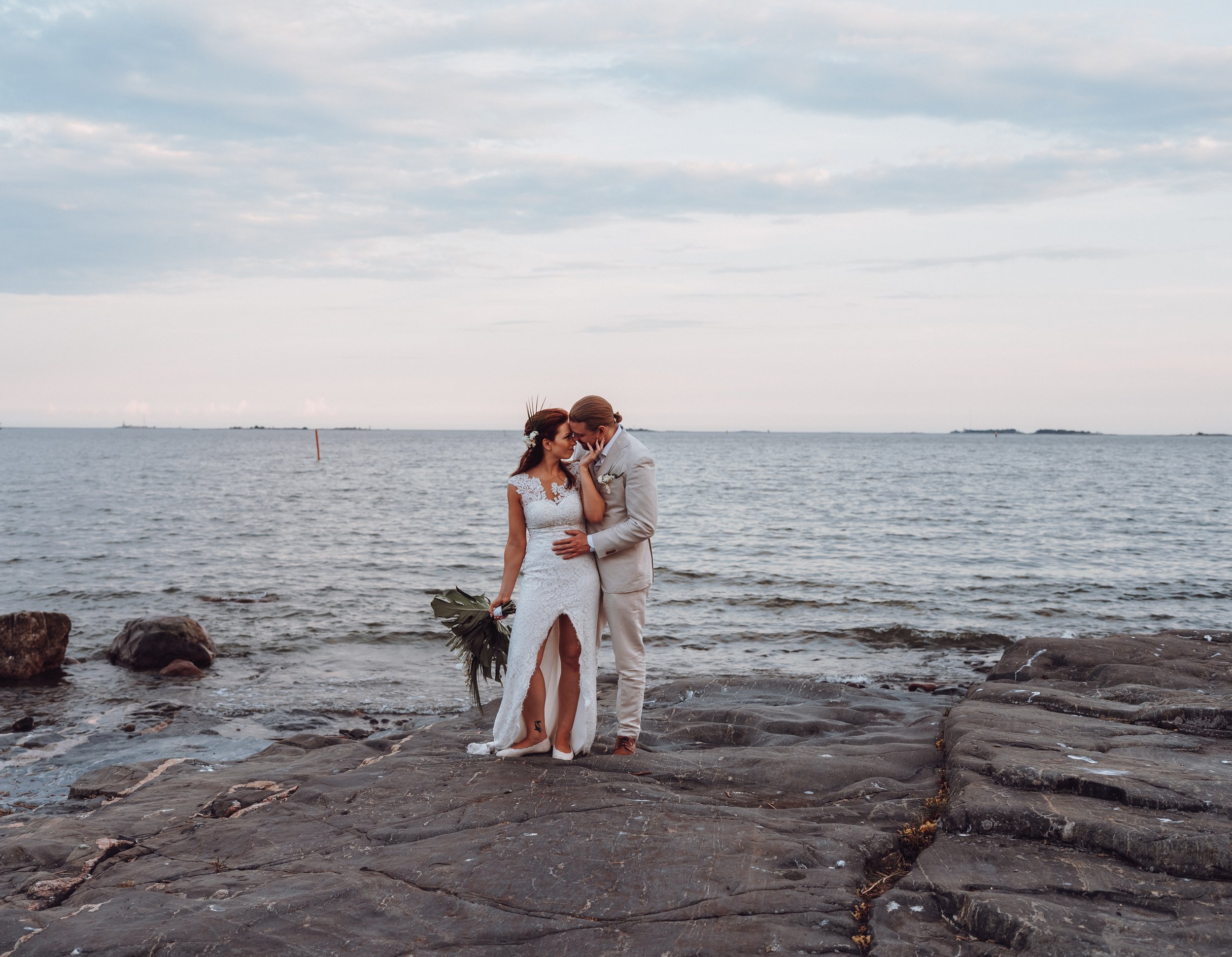 Bride and groom embracing on rocky shore with ocean backdrop