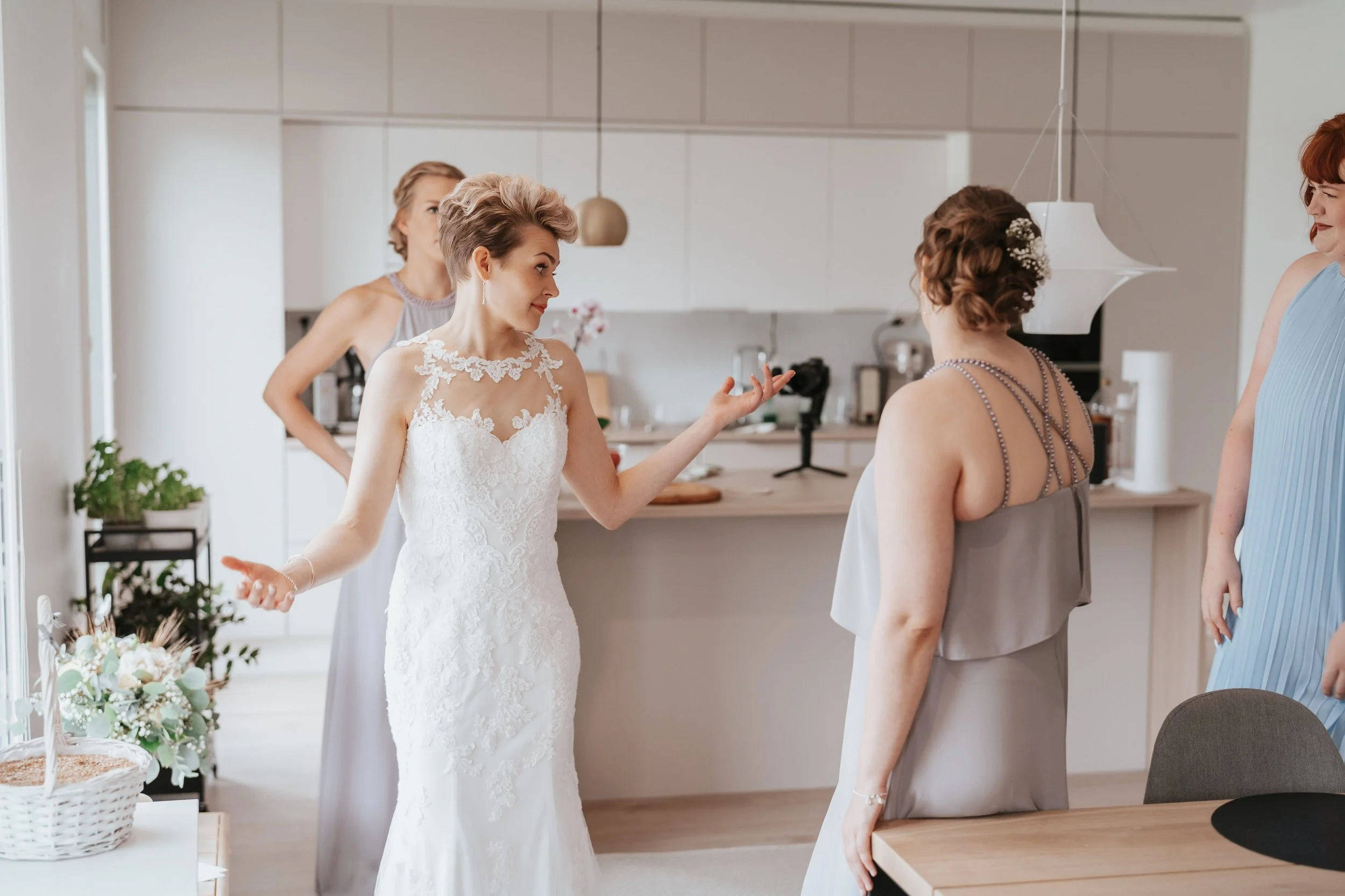 Bride in white lace dress with bridesmaids in a modern kitchen setting