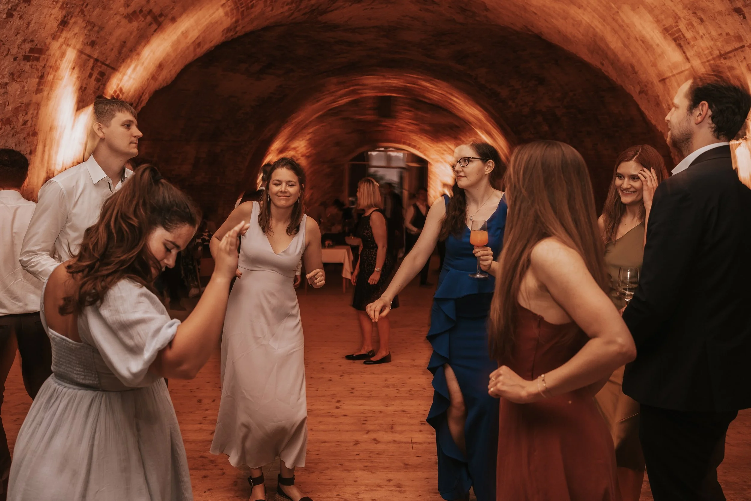 People dancing in a warmly lit event space with arched ceilings, wearing formal attire.