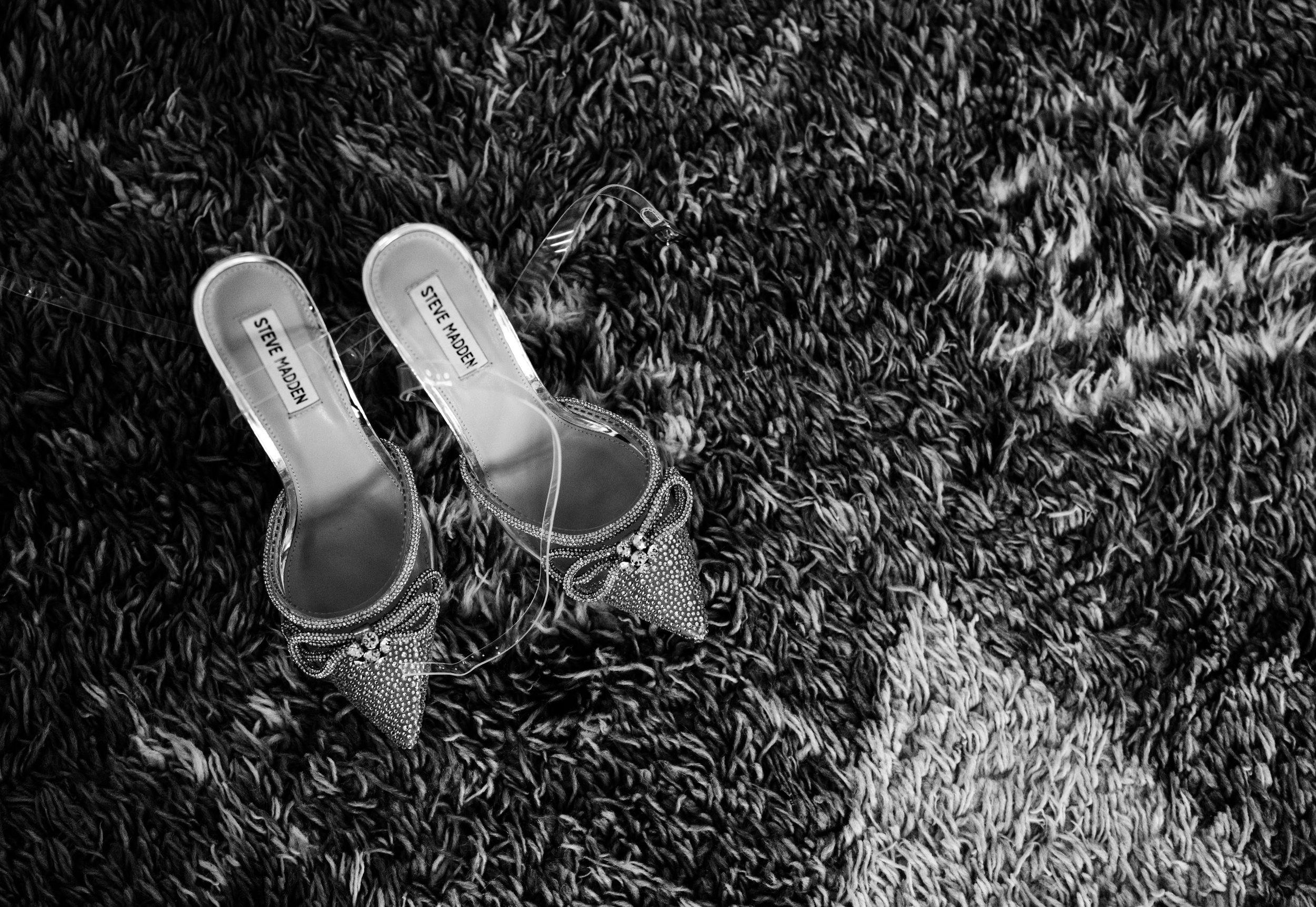 Black and white image of Steve Madden bejeweled high heel shoes on a textured carpet.