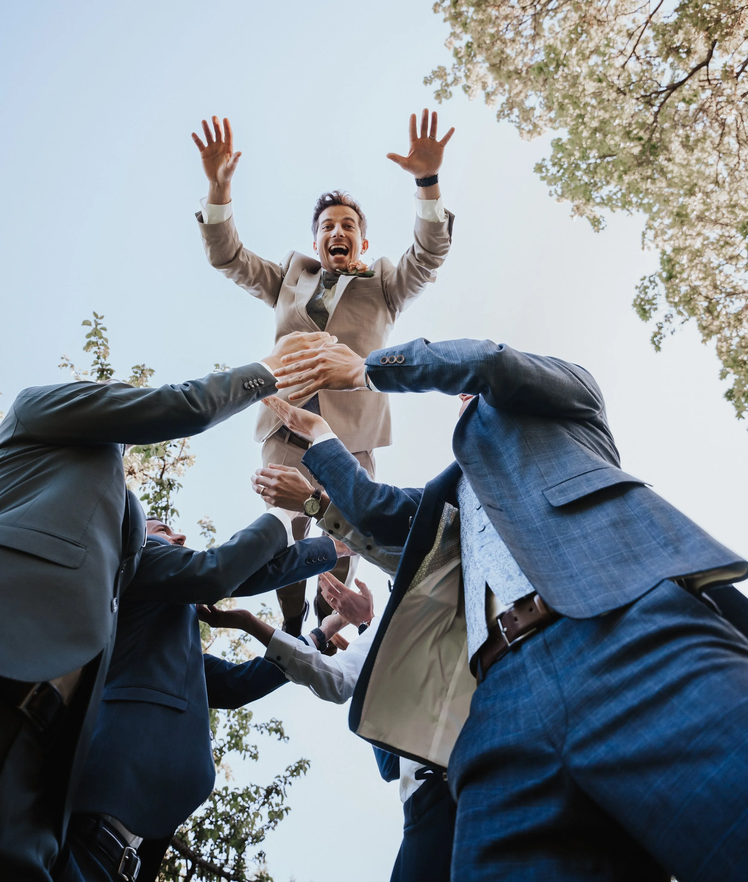 Groom being tossed in the air by groomsmen outdoors