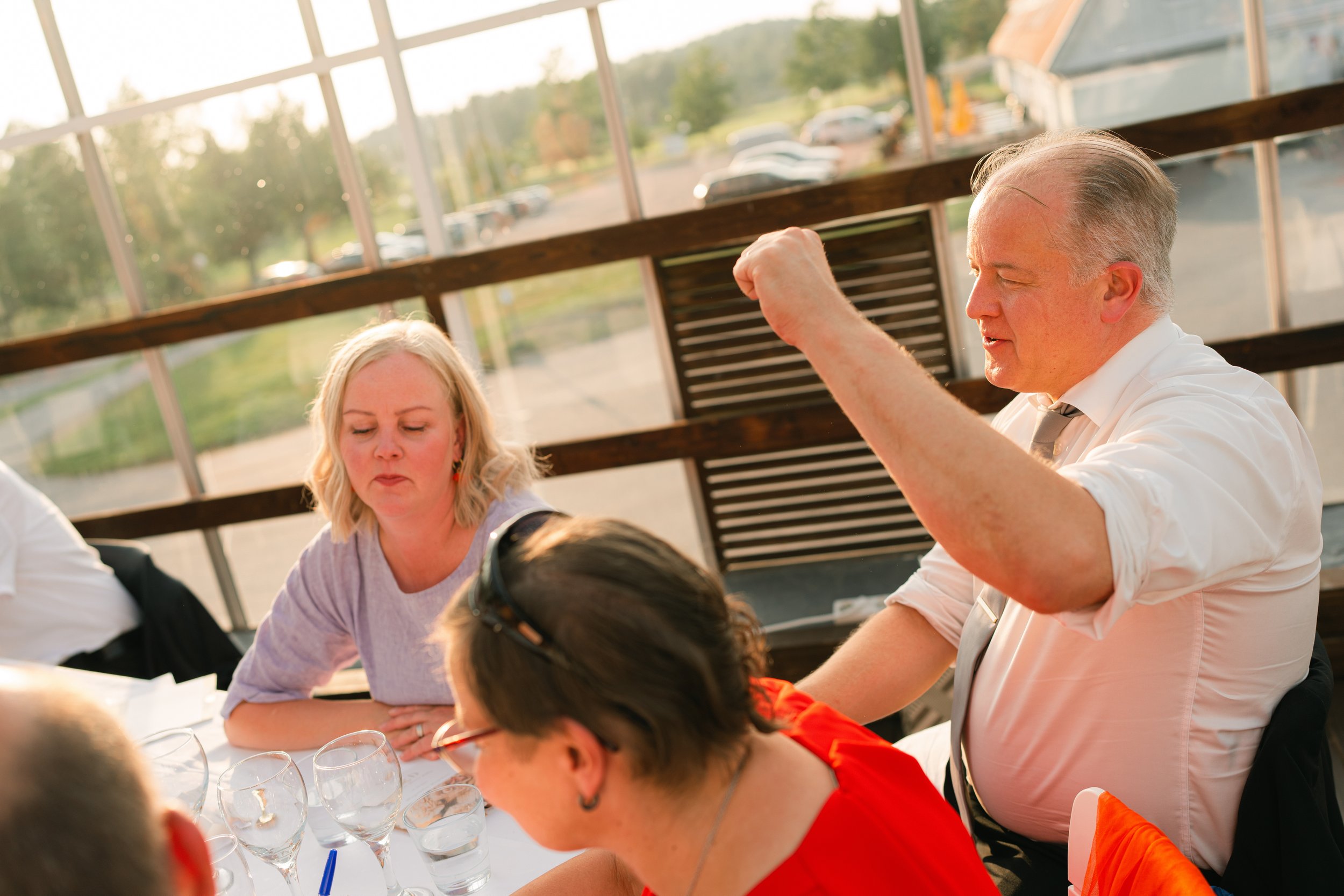 Group of people sitting at a table with drinks, engaged in conversation near a large window.