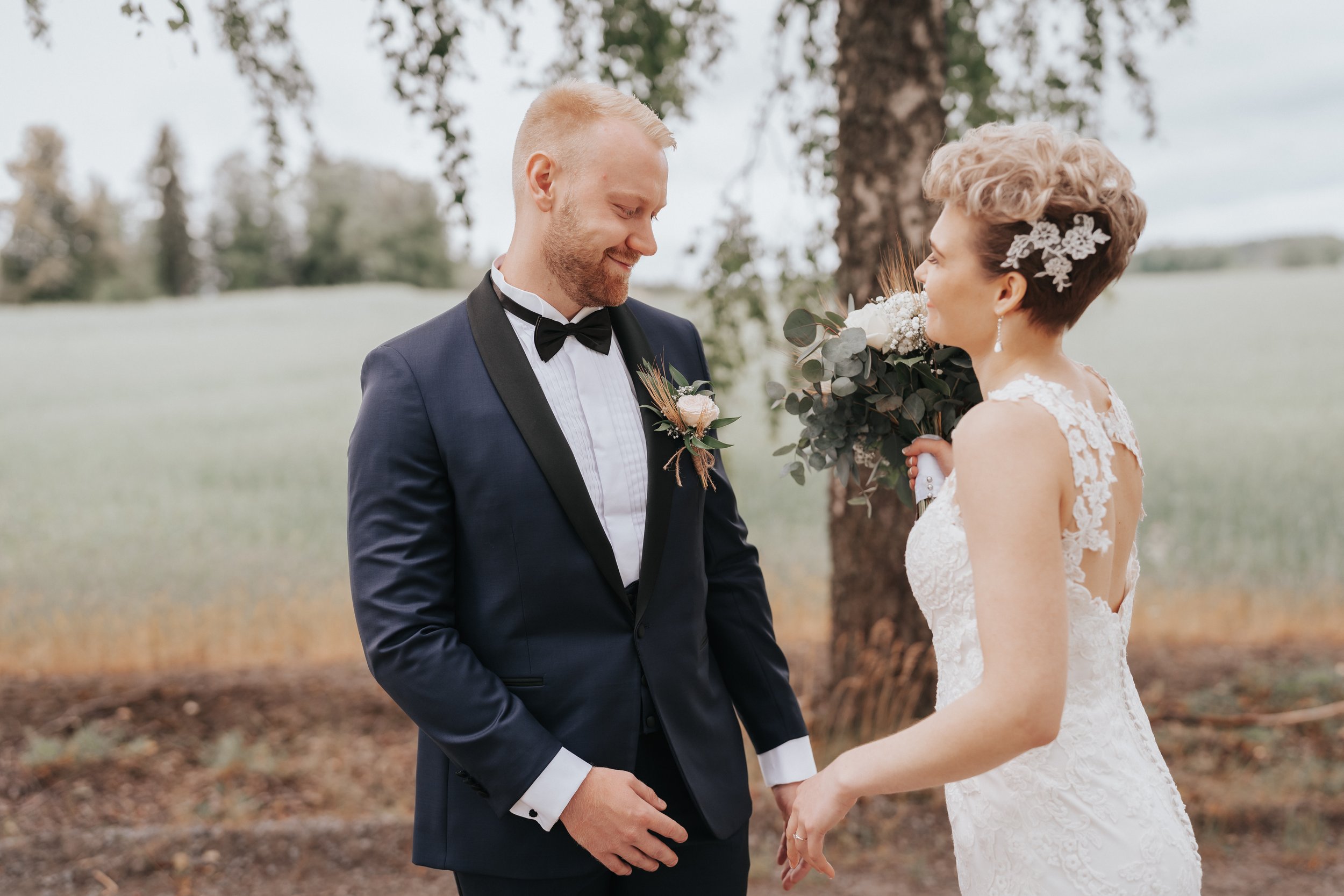 Bride and groom outdoors, bride holding bouquet, standing near tree.