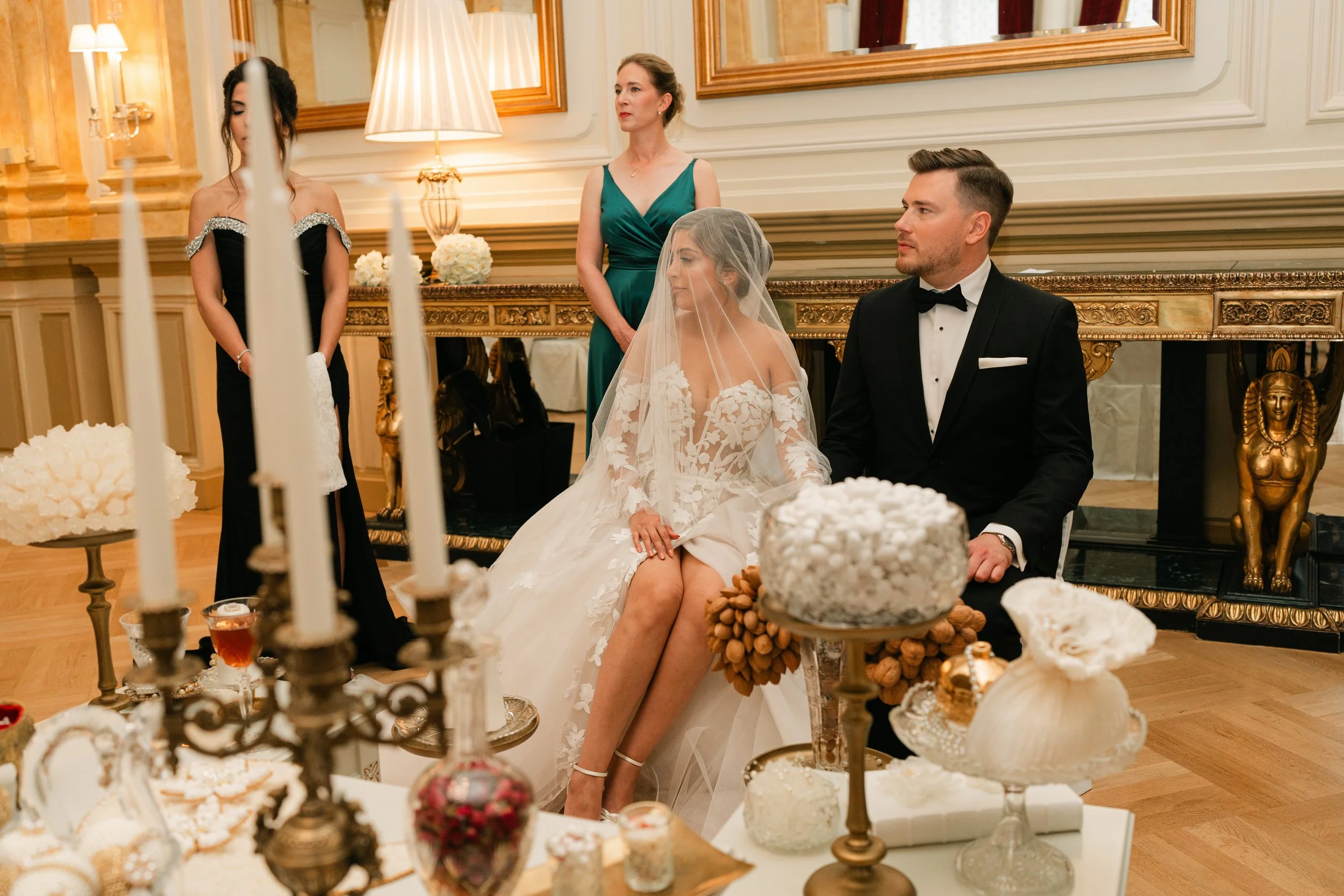 Elegant Persian wedding ceremony with a bride and groom seated, surrounded by traditional decor and guests, in an opulent setting.