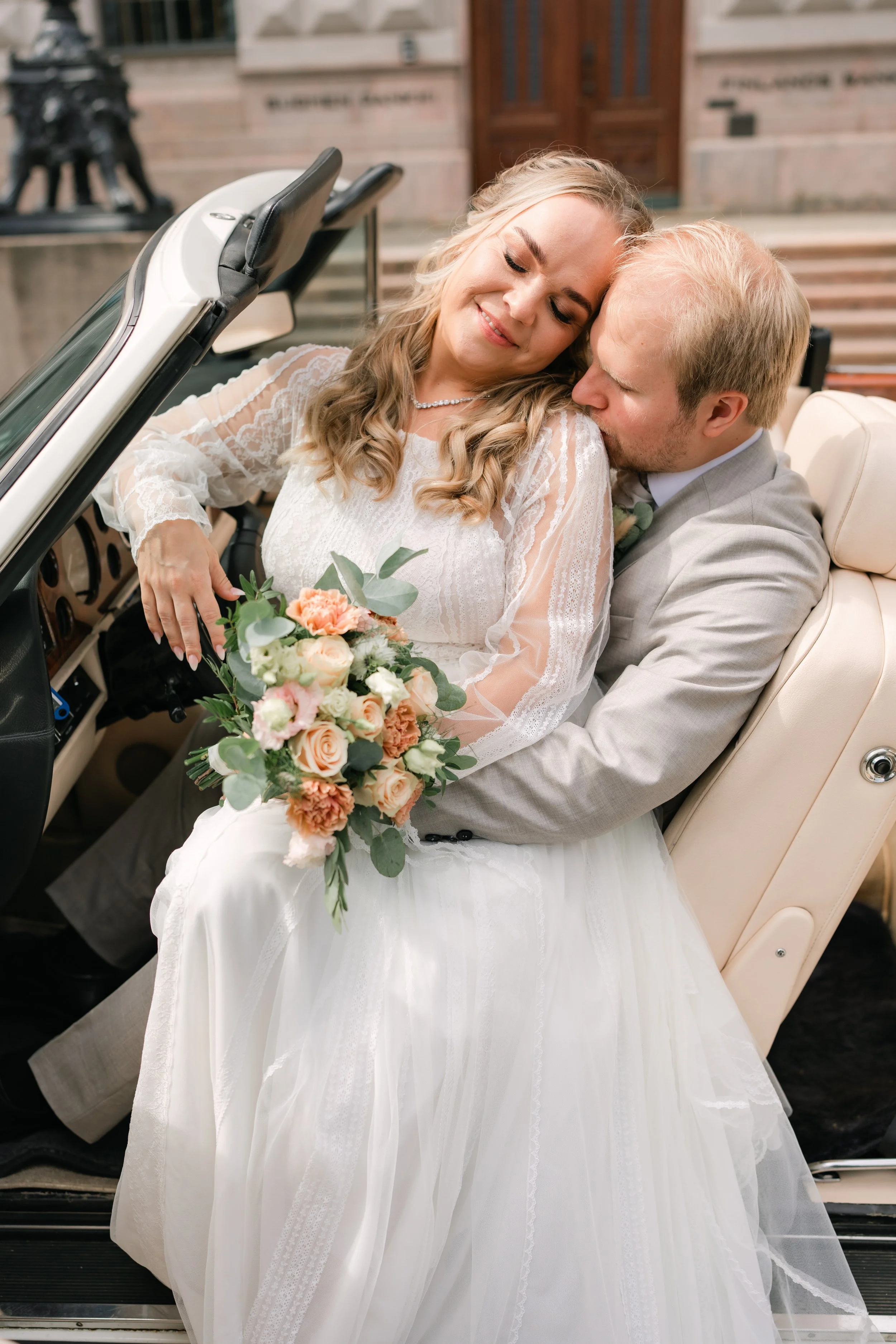 Bride and groom sitting in a convertible car, bride holding a flower bouquet