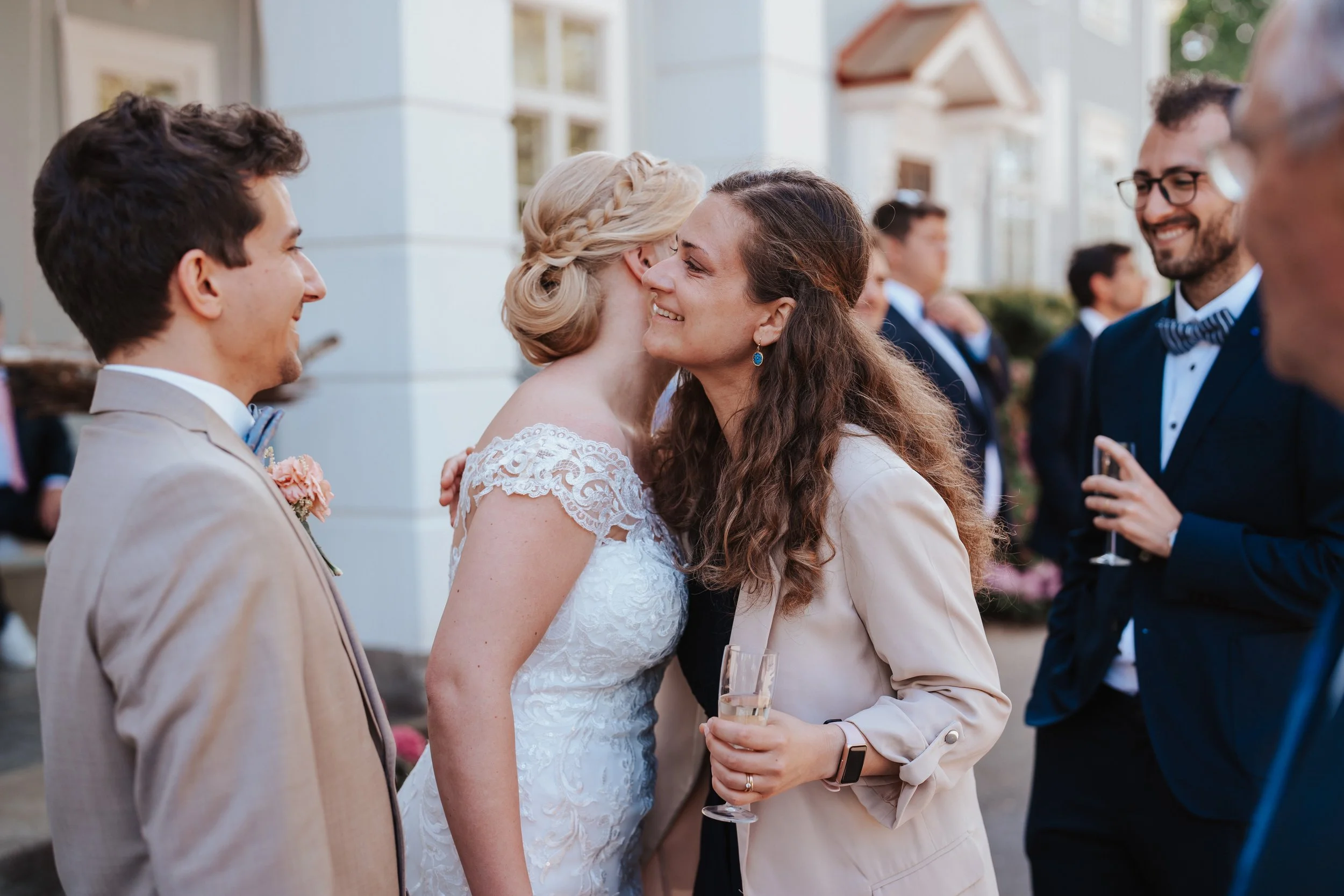 Wedding scene with bride hugging guest, people in formal attire, outdoor reception