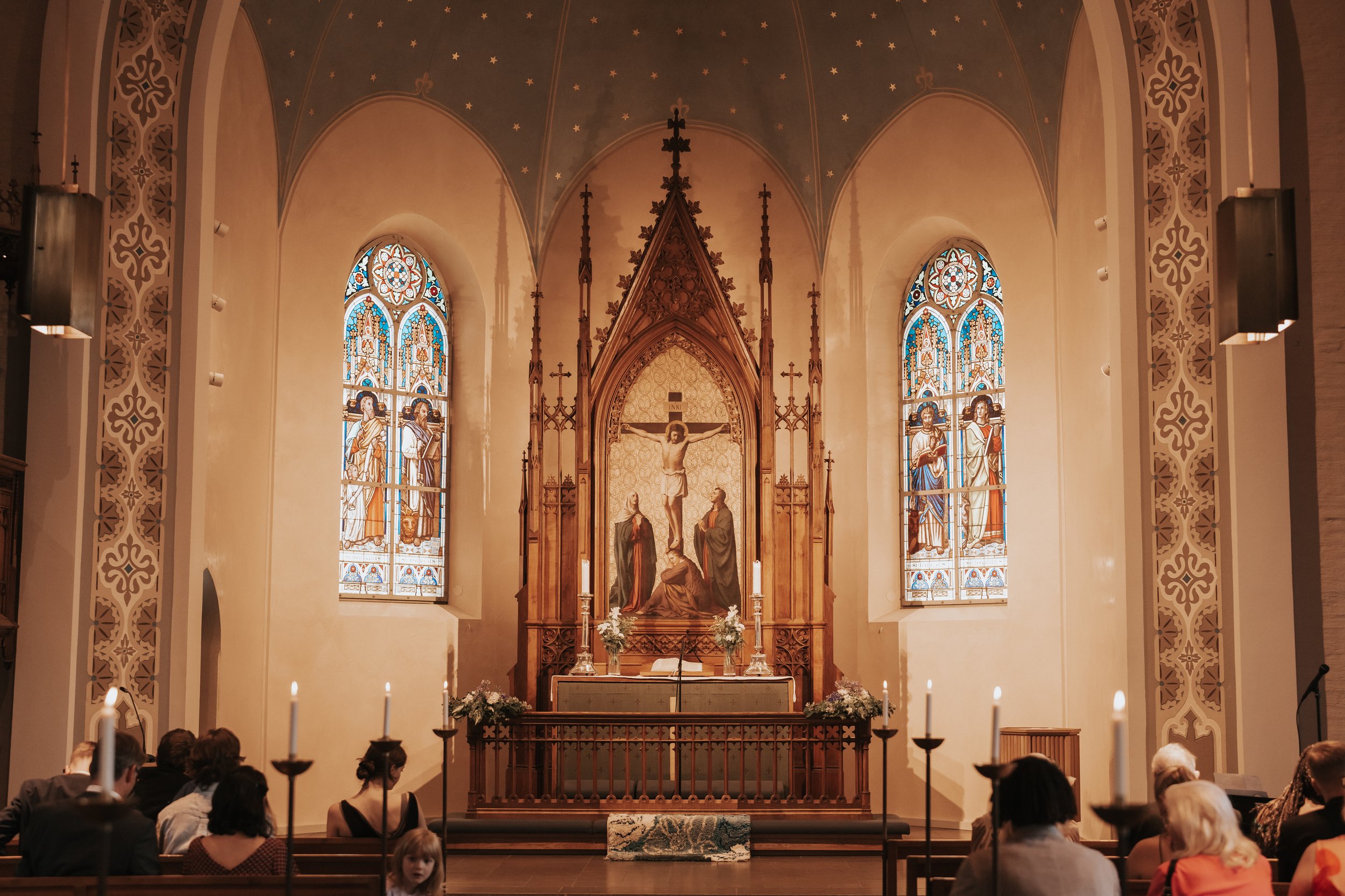 Interior of a church with stained glass windows, altar, and people seated.
