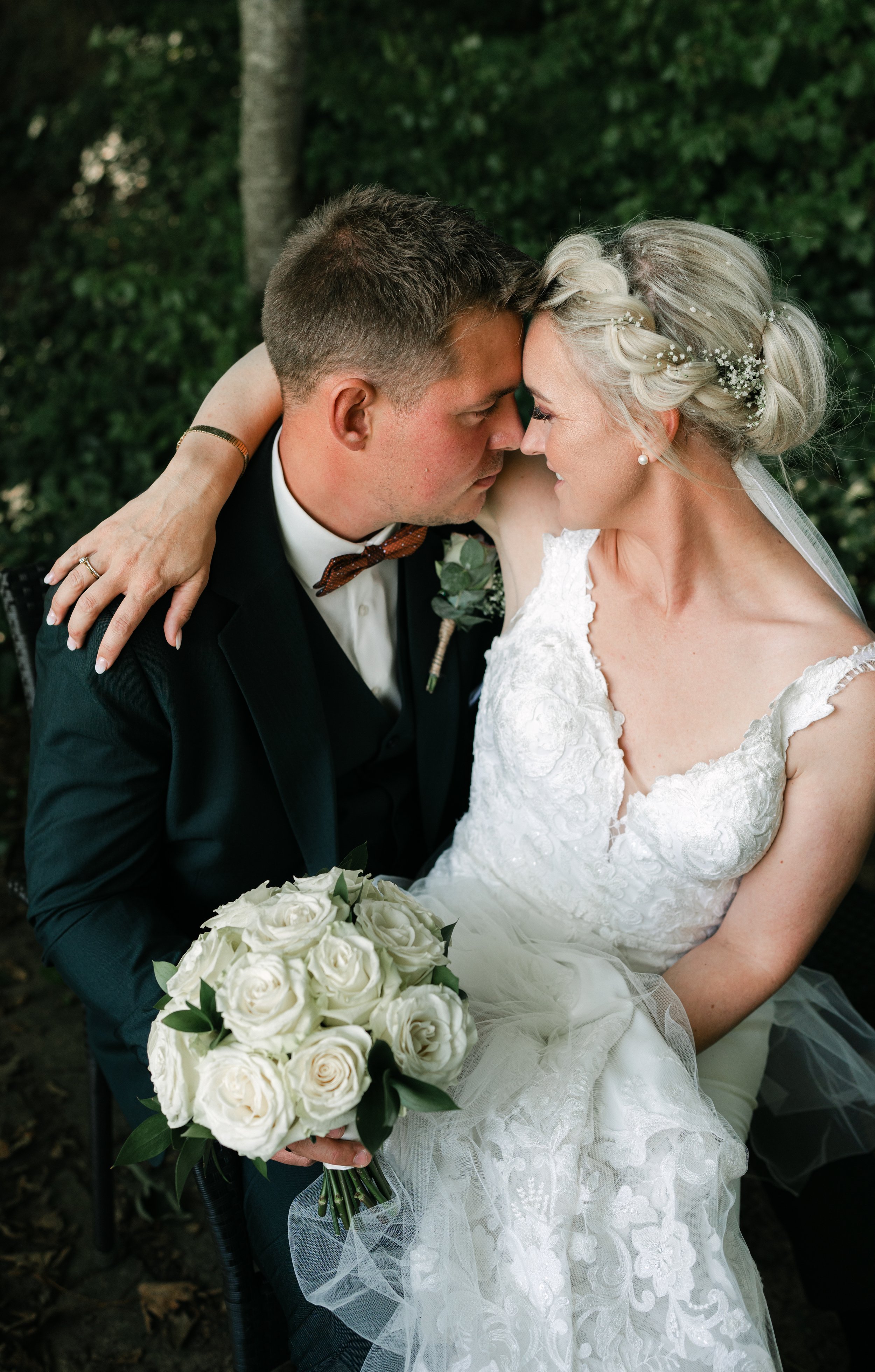 Bride and groom embracing and holding a bouquet of white roses.