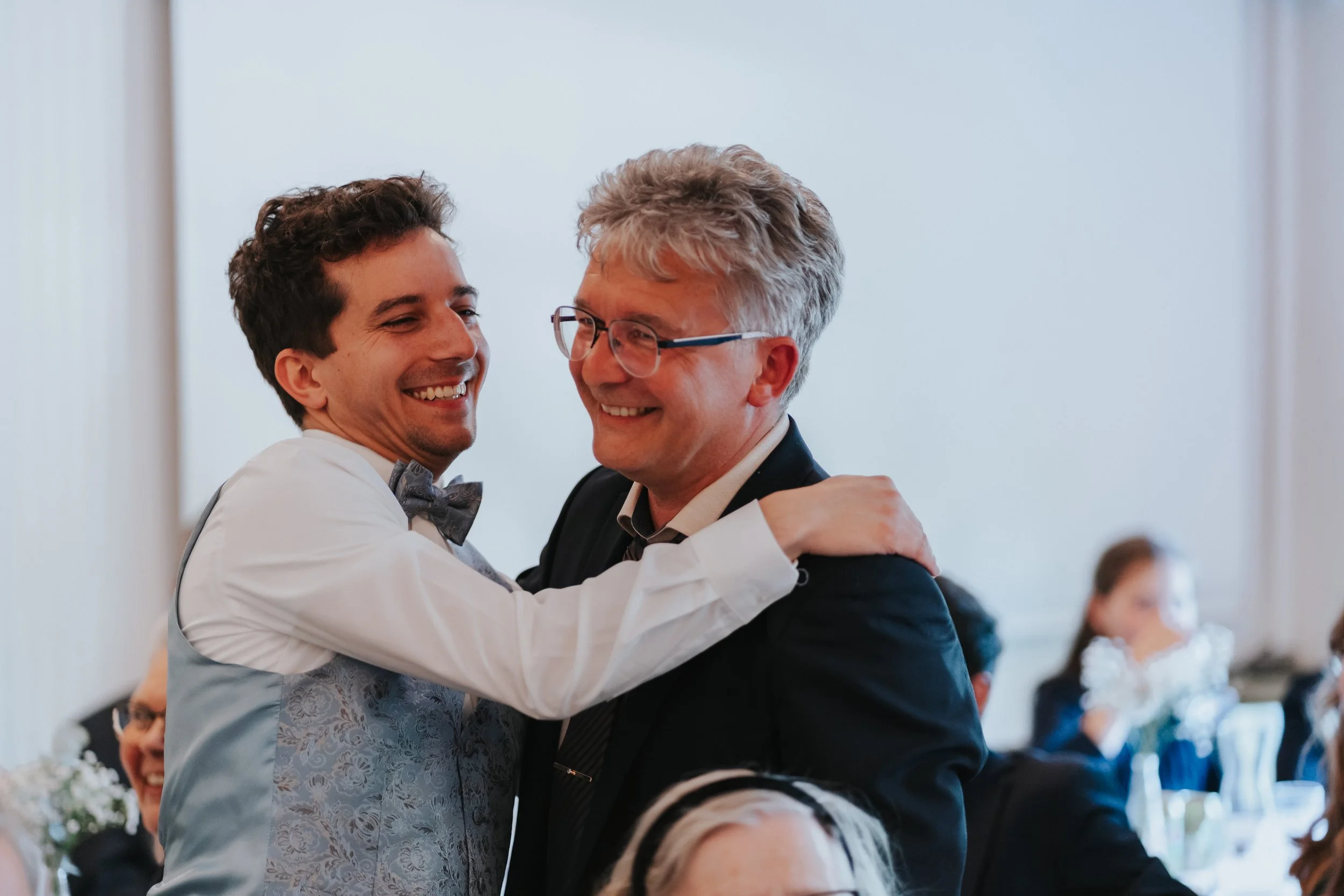 Two men smiling and hugging in a formal setting.