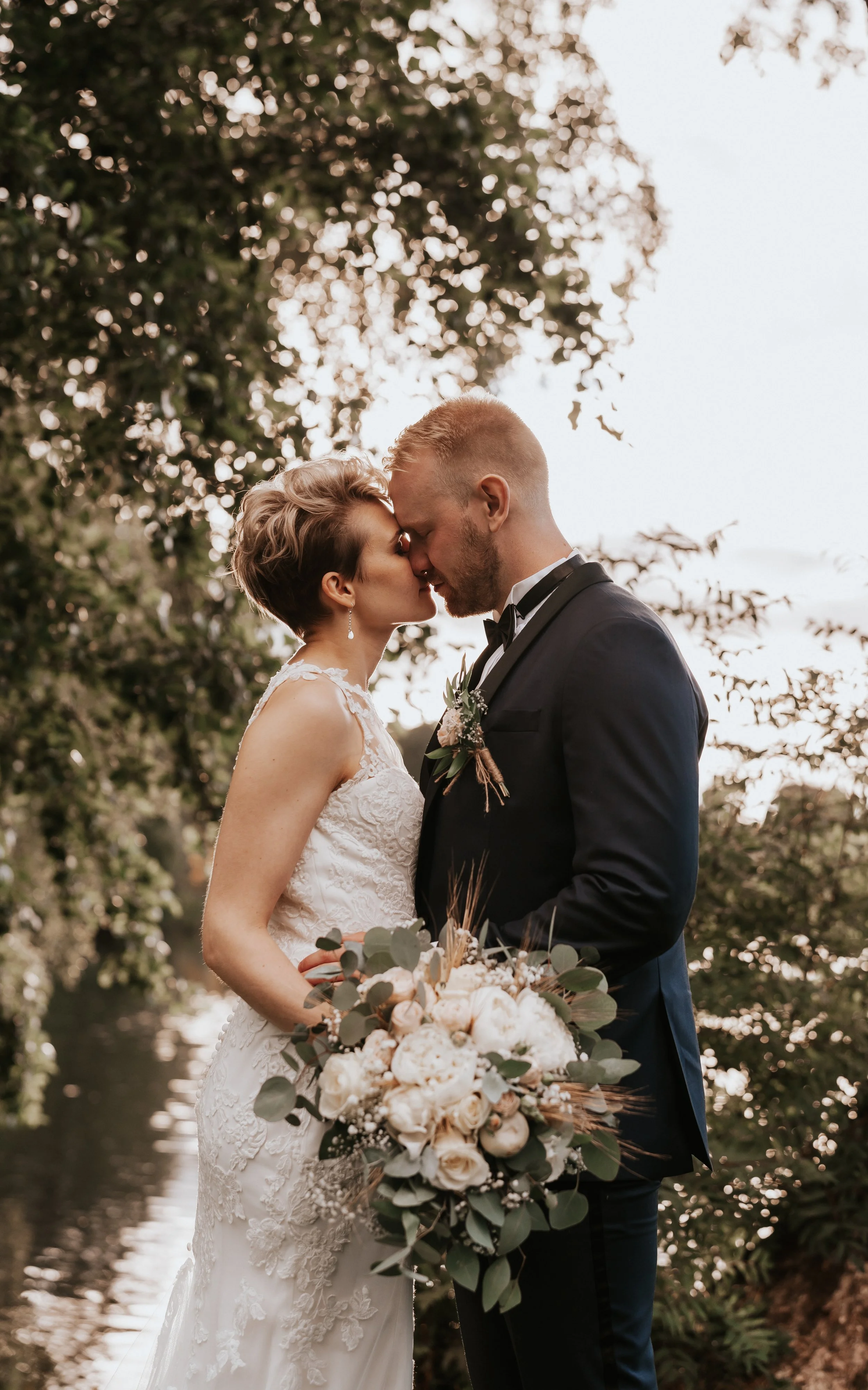 Bride and groom kissing outdoors with bouquet