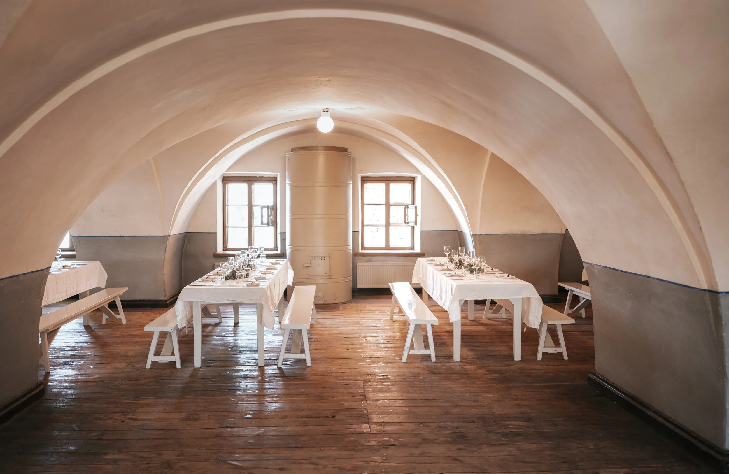 Rustic dining room with arched ceiling, wood floor, and tables set for a meal.