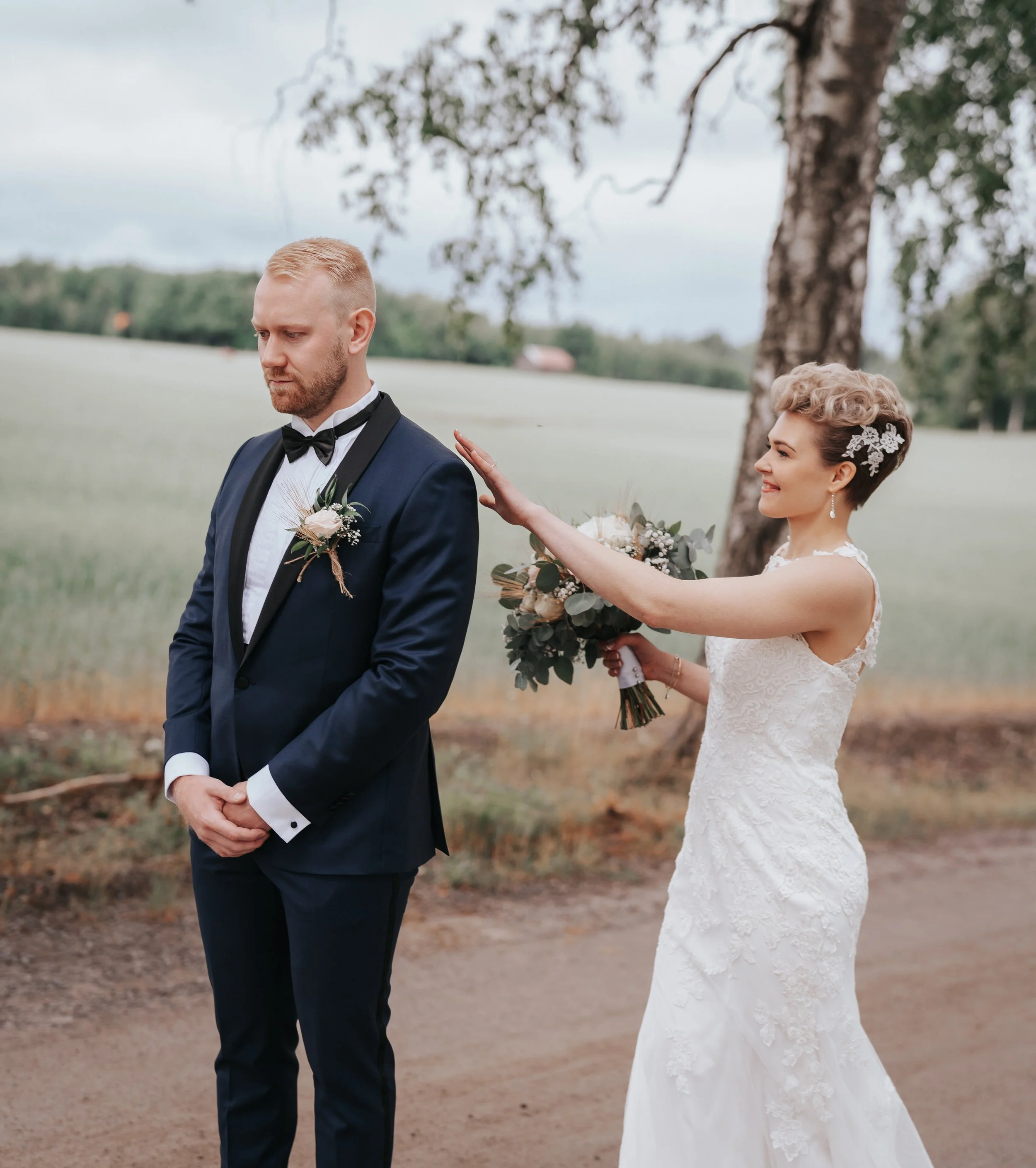 Bride touching groom's shoulder before first look in outdoor setting.