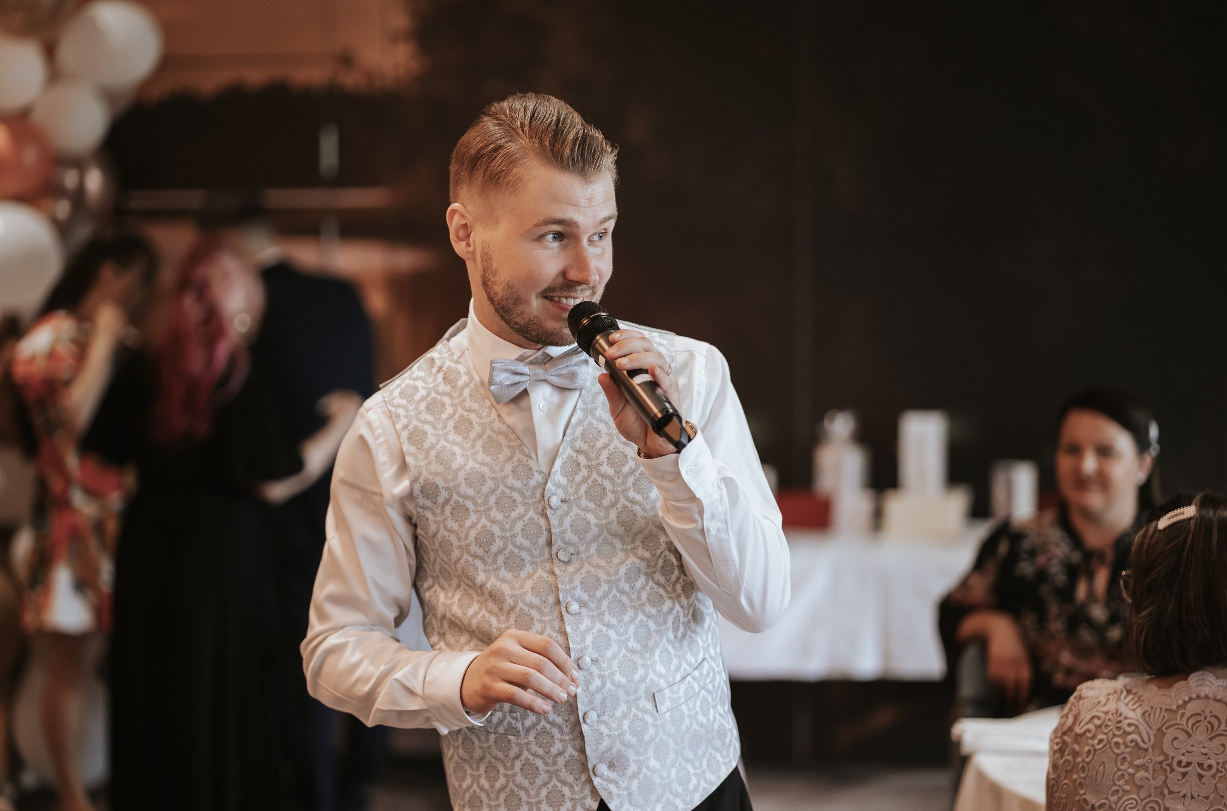 Man in stylish vest speaking into microphone at event