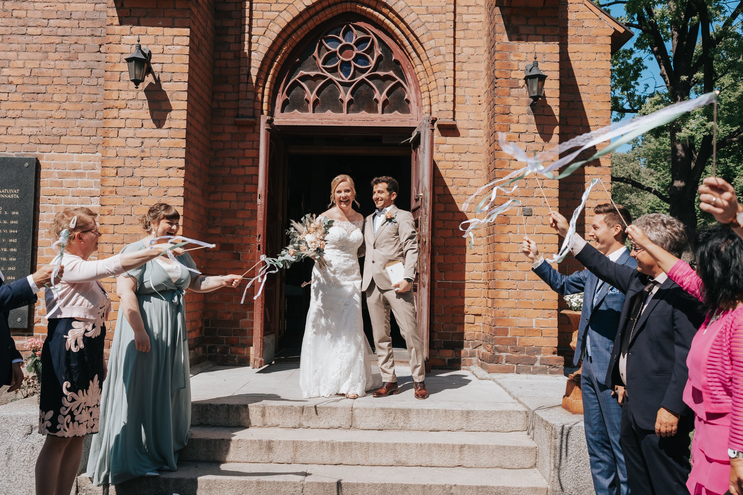 Bride and groom exiting a church with guests waving ribbons.