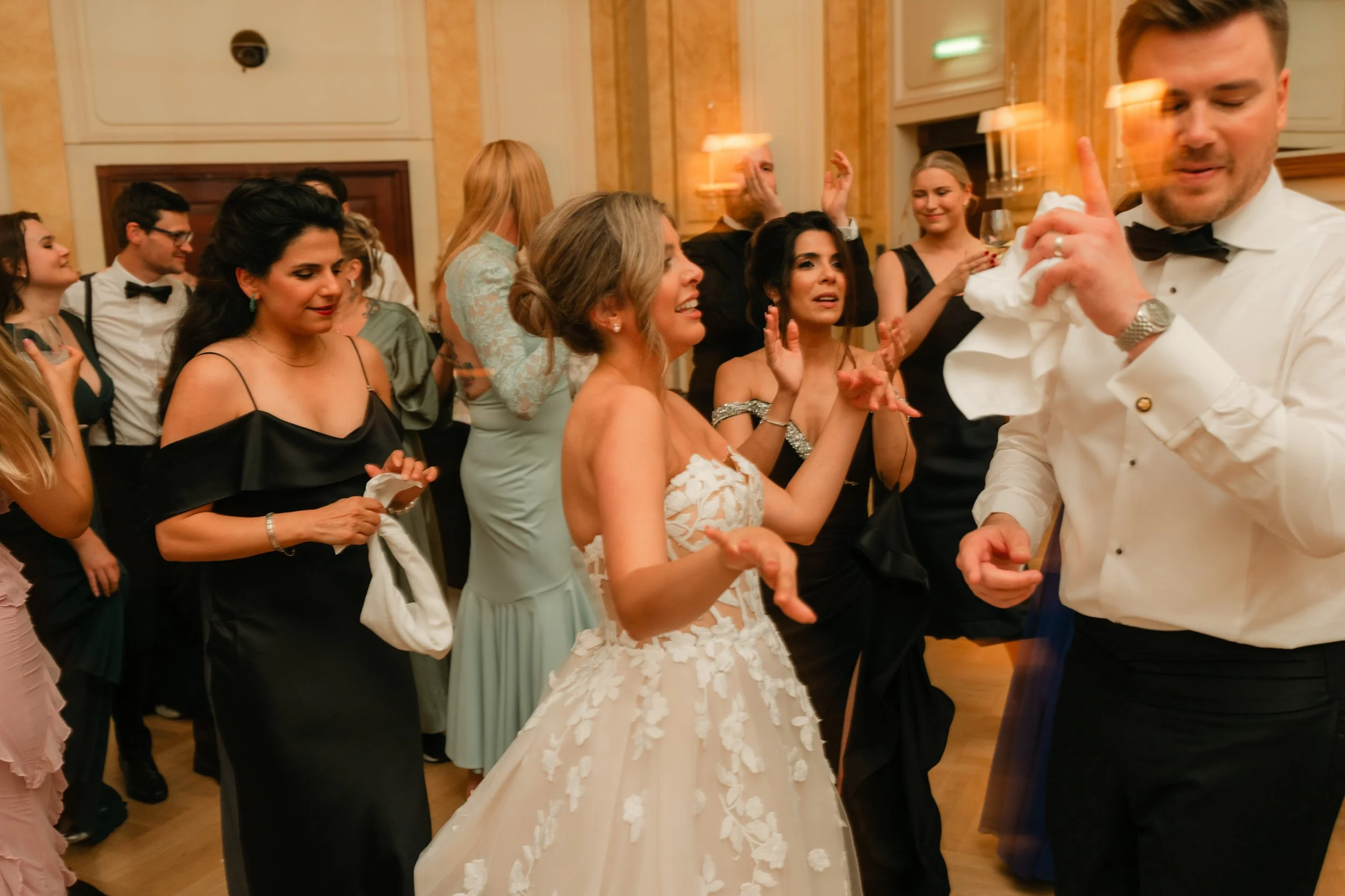 People dancing at a formal event, including a bride in a white dress and guests in evening attire.