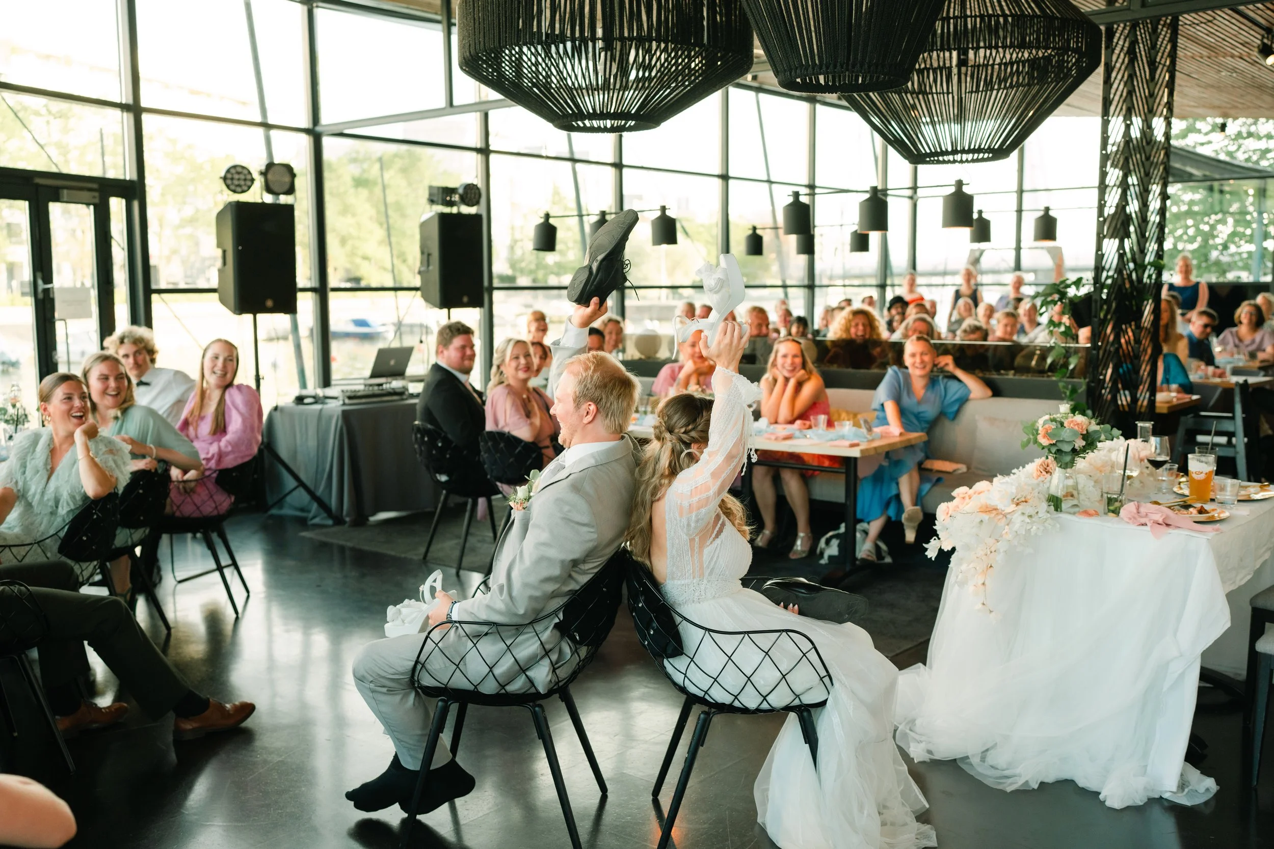 Bride and groom playing wedding shoe game indoors with laughing guests around