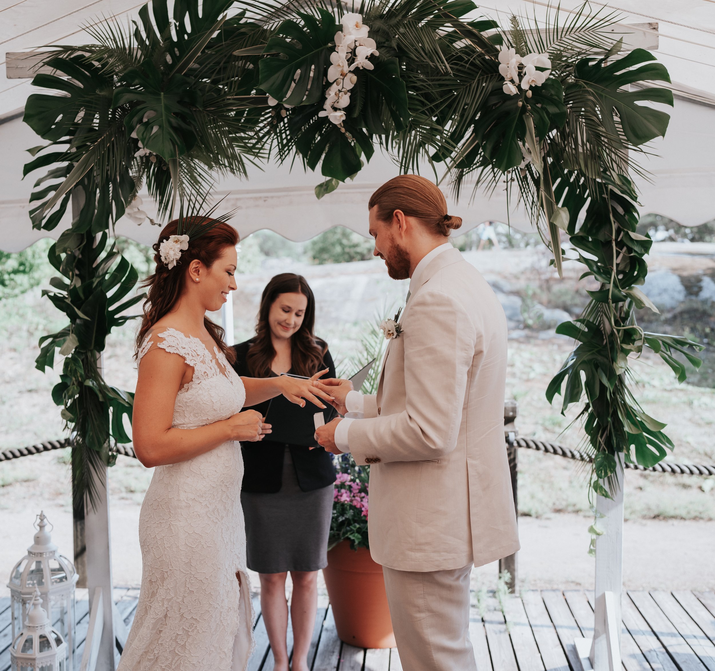 Bride and groom exchanging rings under a floral arch at a wedding ceremony with officiant.