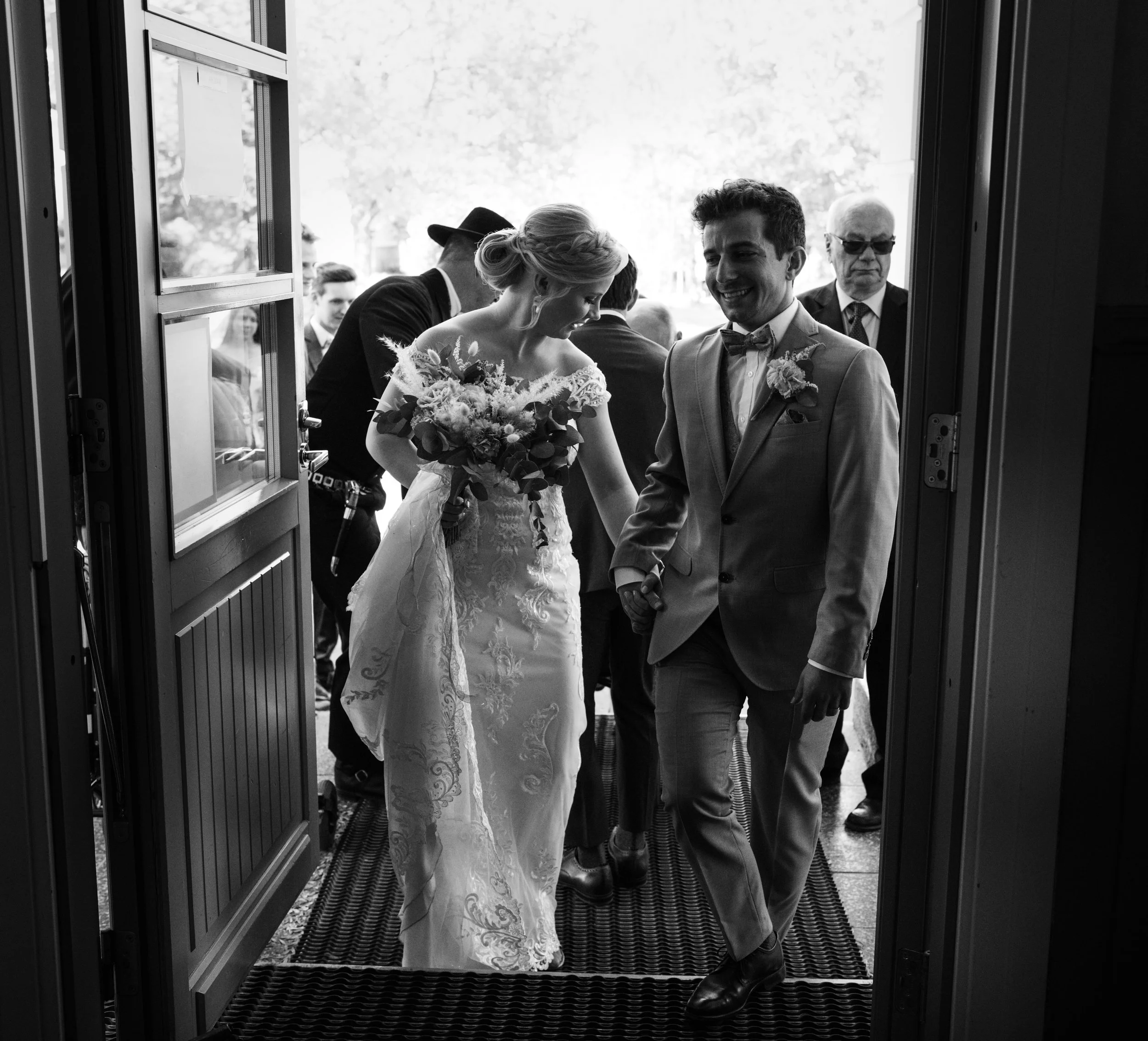 Bride and groom smiling as they exit a building, black and white photo, wedding scene.