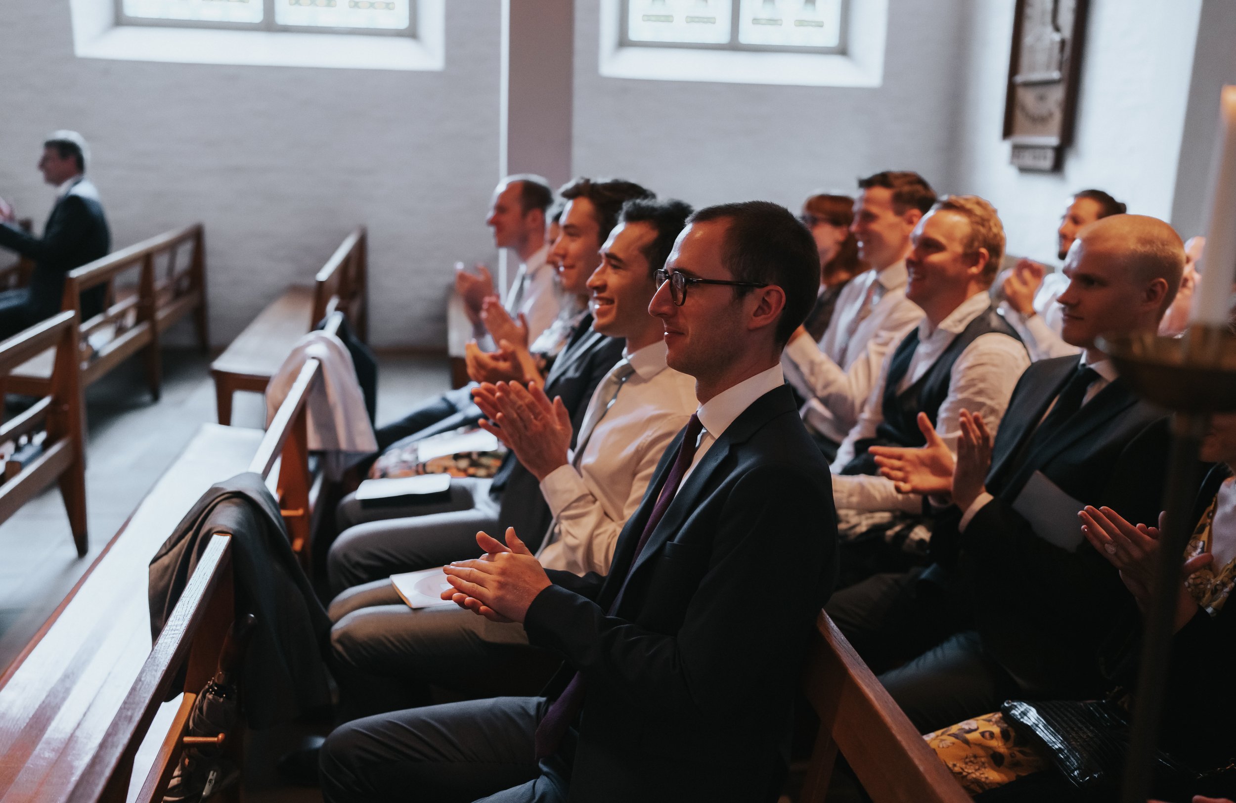 Group of people in formal attire sitting in church pews clapping enthusiastically.