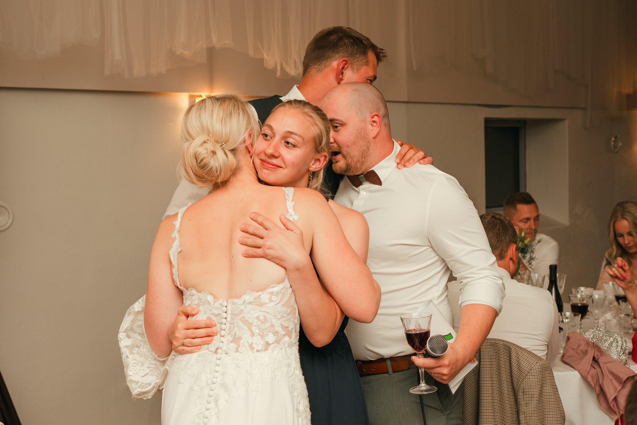 Group hug at event, woman in wedding dress, people holding wine glasses