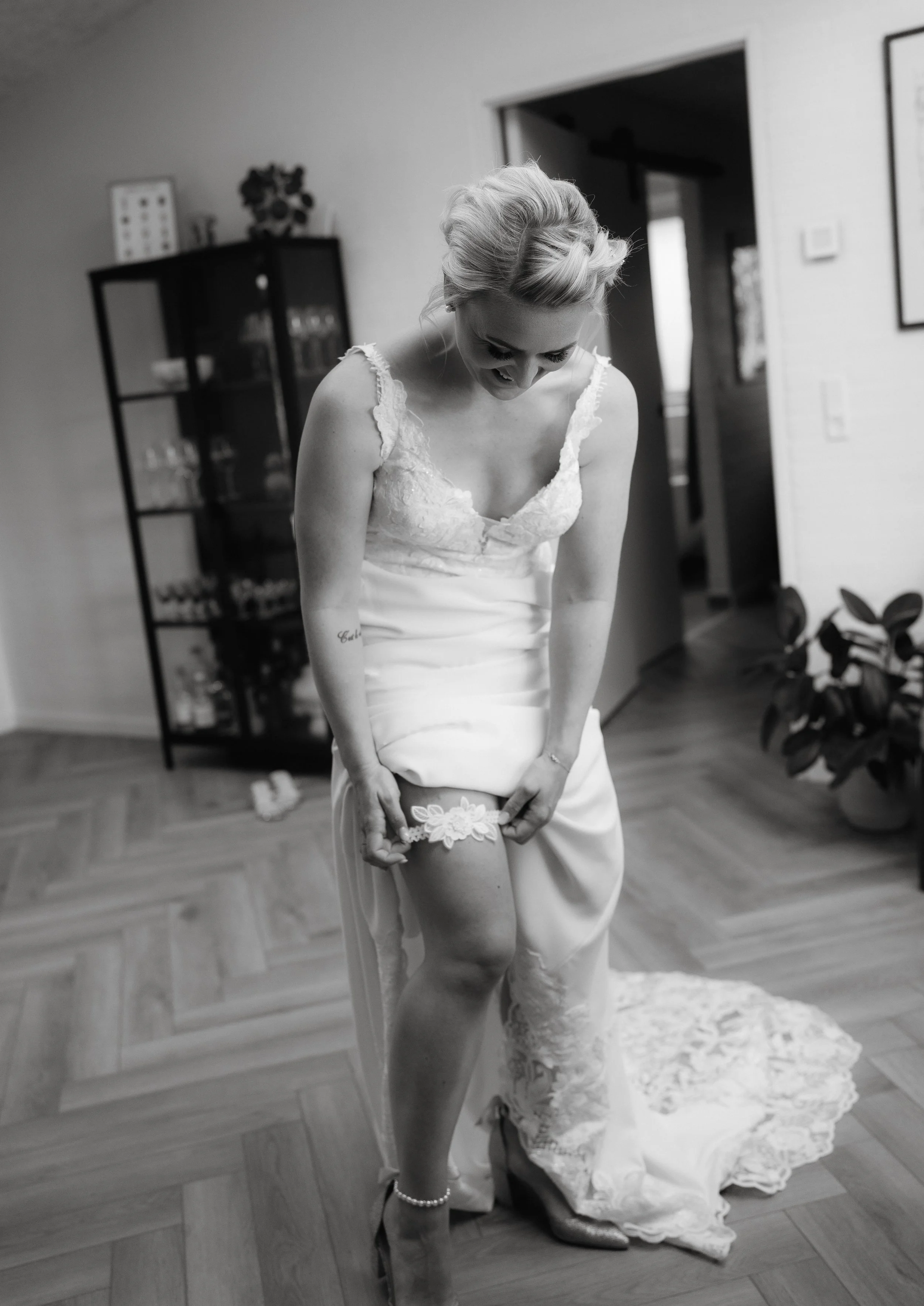Bride adjusting wedding garter in a white dress, indoor setting