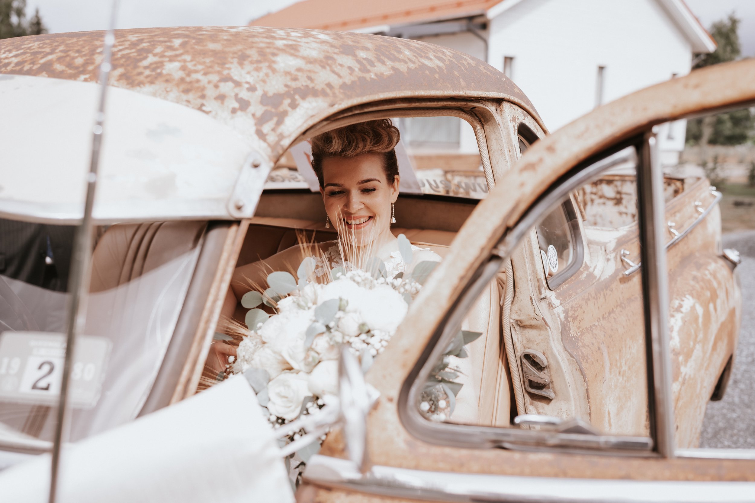 Bride holding bouquet in vintage car, smiling