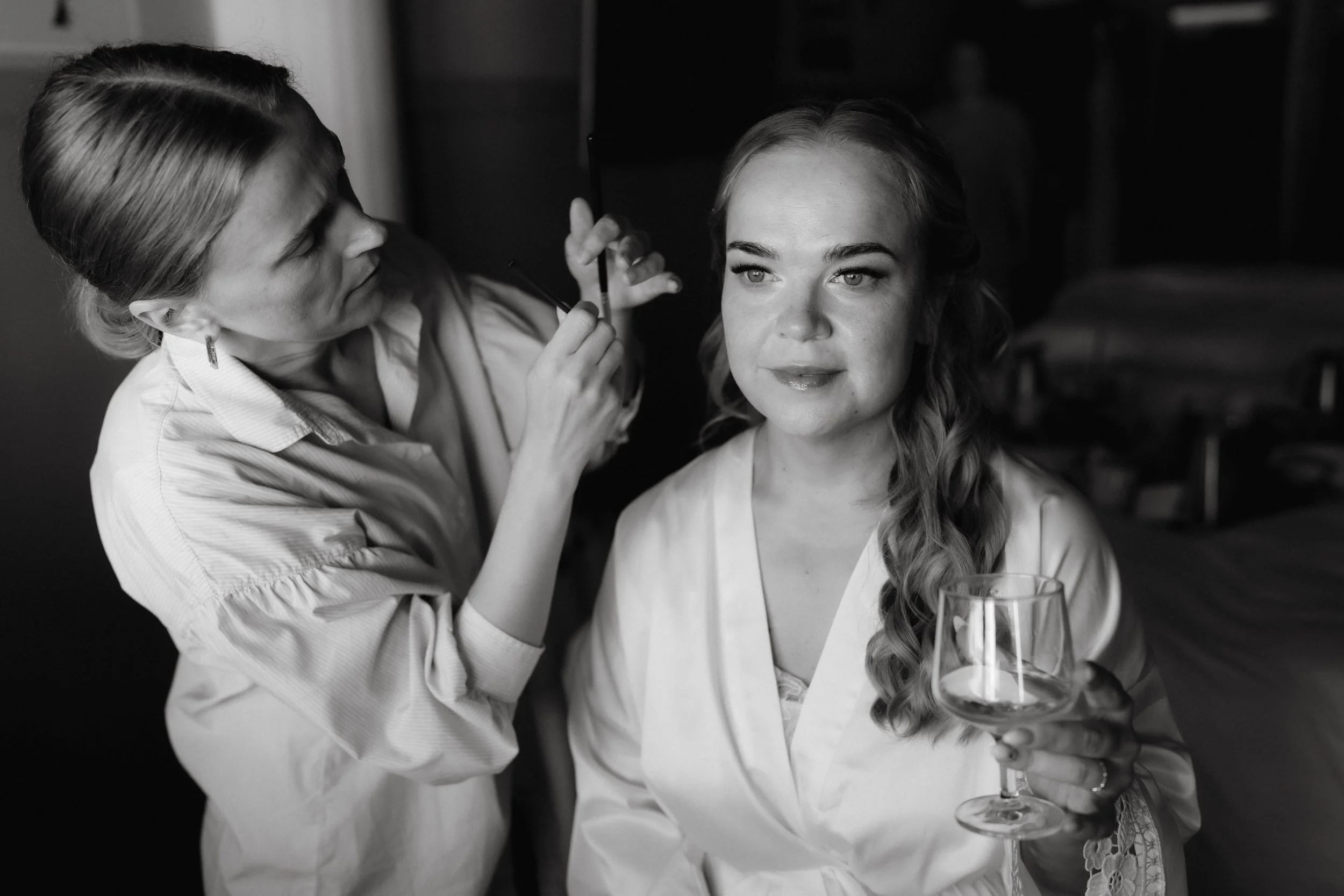 Black and white photo of a woman holding a wine glass while another woman styles her hair.